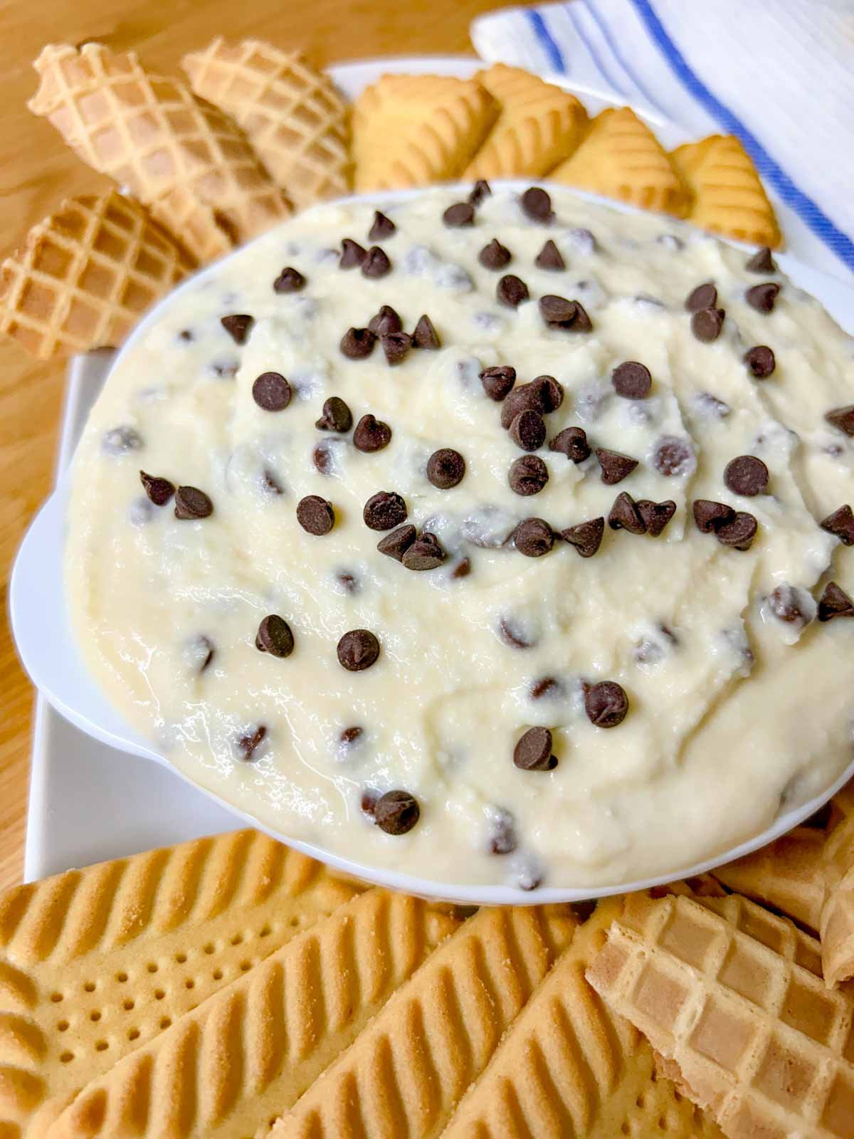 a white bowl is filled with cannoli dip and there are cookies around the bowl.