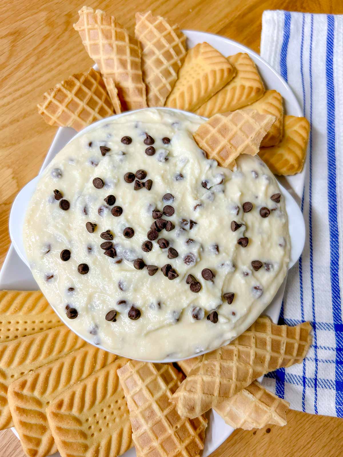 a white bowl is filled with cannoli dip and there are cookies around the bowl. a cookie is dipped
