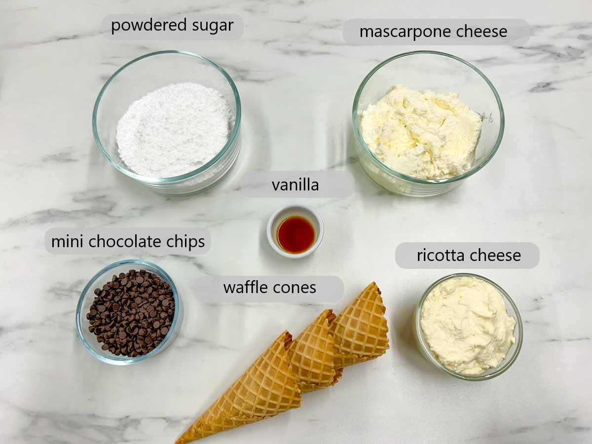 kitchen counter with bowls with ingredients and text overlays reading powdered sugar, mascarpone cheese, mini chocolate chips, vanilla, ricotta cheese and waffle cones
