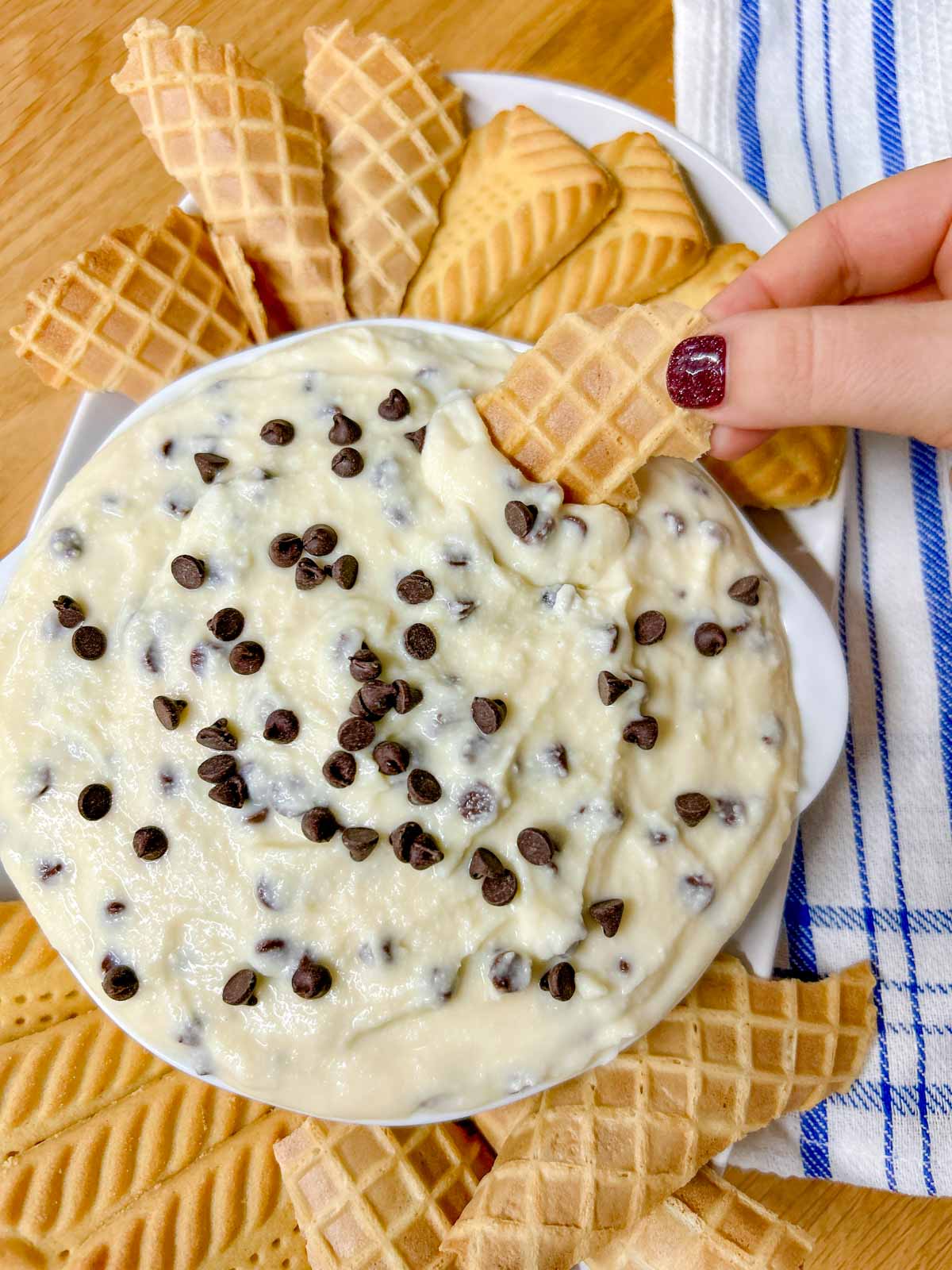 a white bowl is filled with cannoli dip and there are cookies around the bowl. one cookie is dipped in