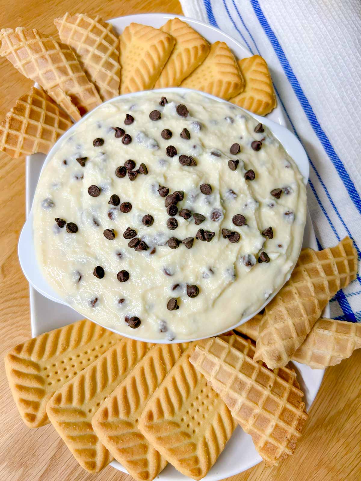 a white bowl is filled with cannoli dip and there are cookies around the bowl.