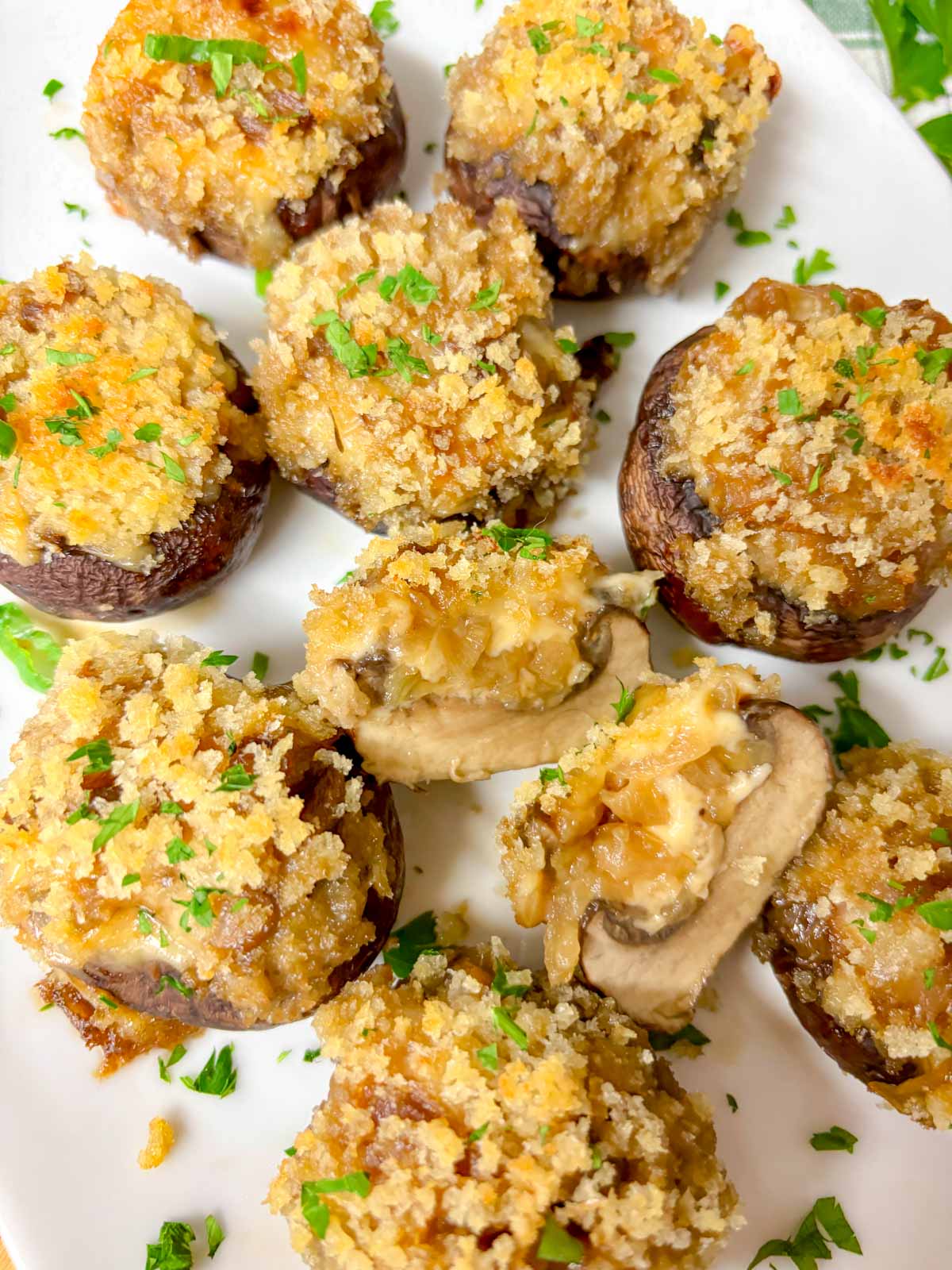 a white plate is filled with French onion stuffed mushrooms and garnished with parsley. one is cut in half