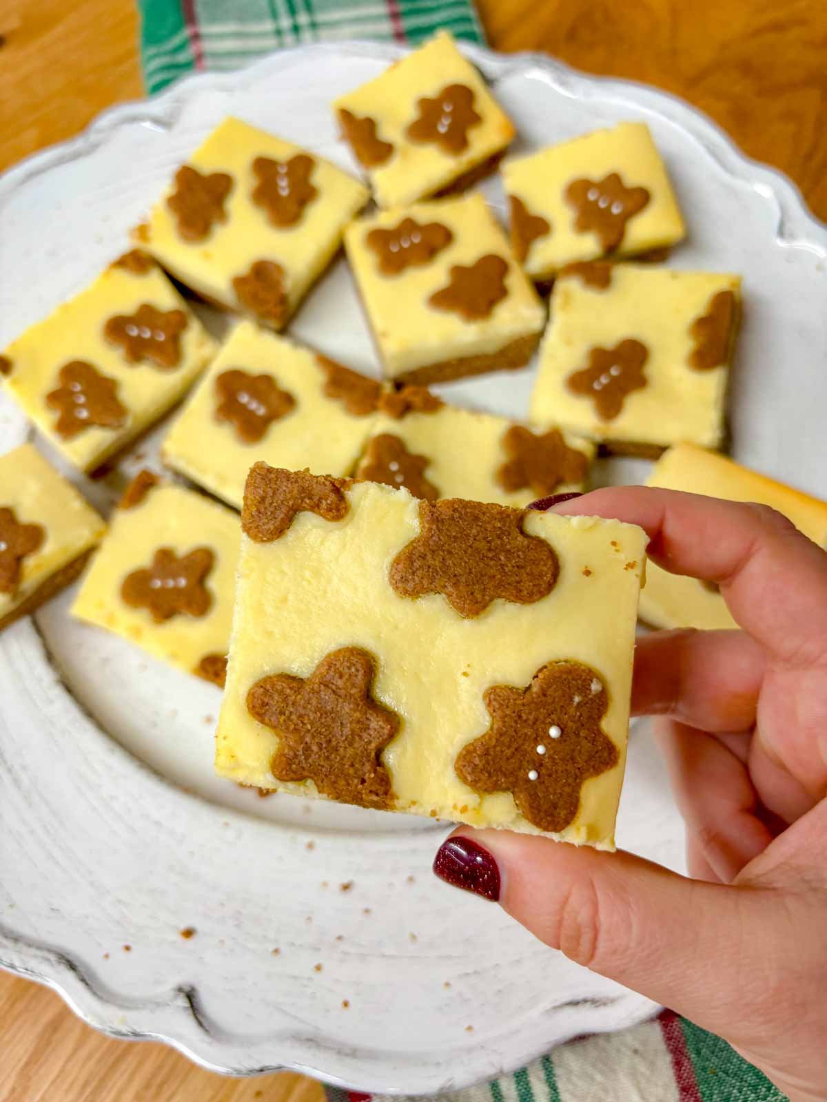 a white plate is filled with gingerbread cookie bars. one is held close to camera