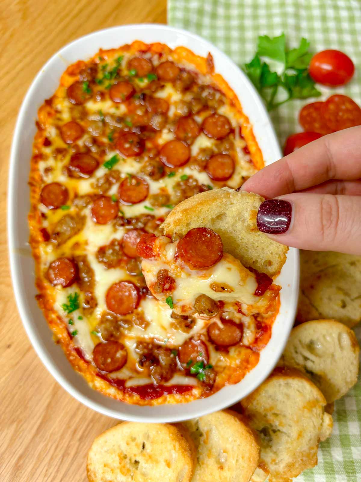 a white baking tray is filled with hot honey pepperoni sausage pizza dip. a piece of baguette is dipped