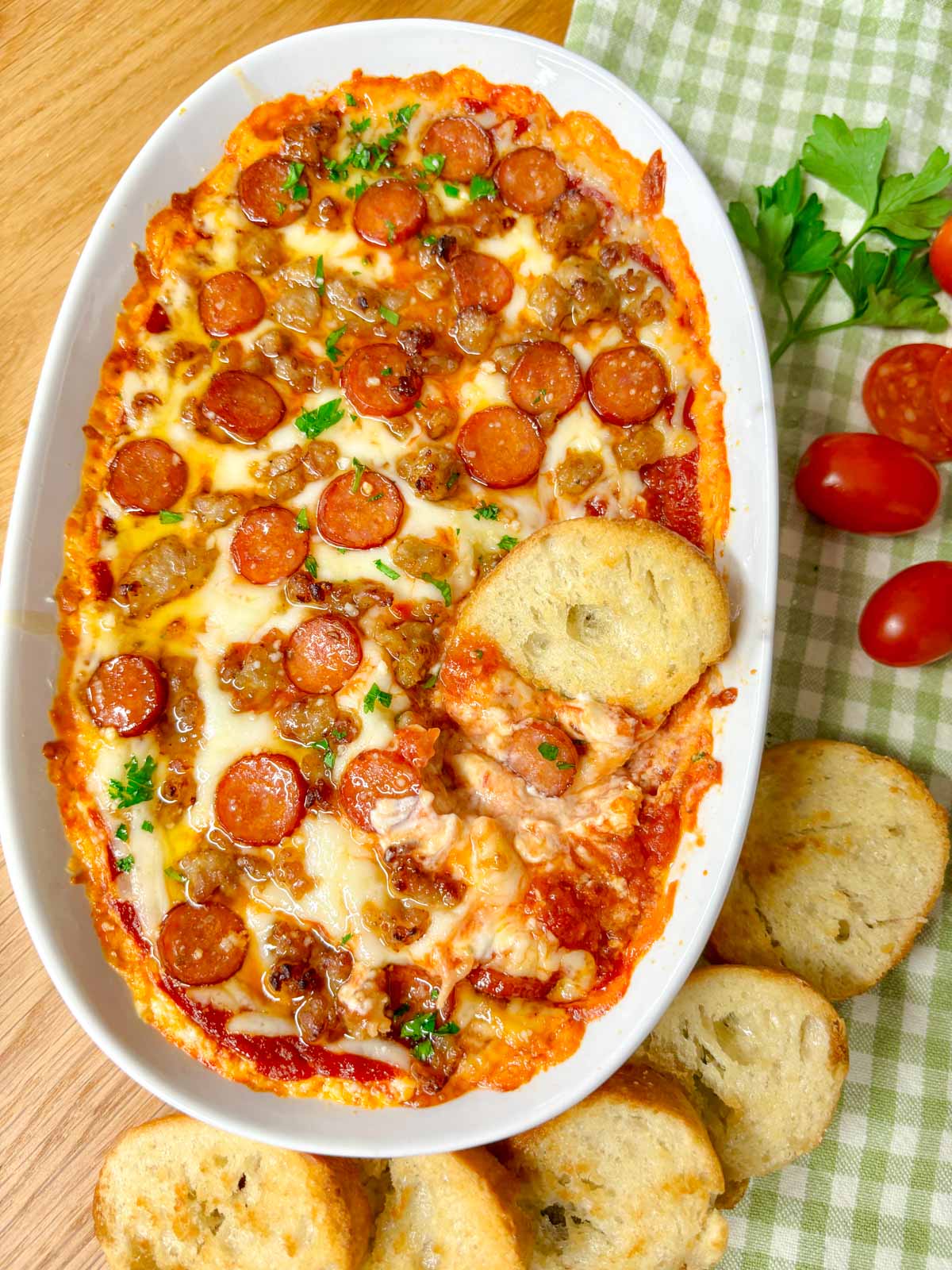 a white baking tray is filled with hot honey pepperoni sausage pizza dip. a piece of baguette is dipped