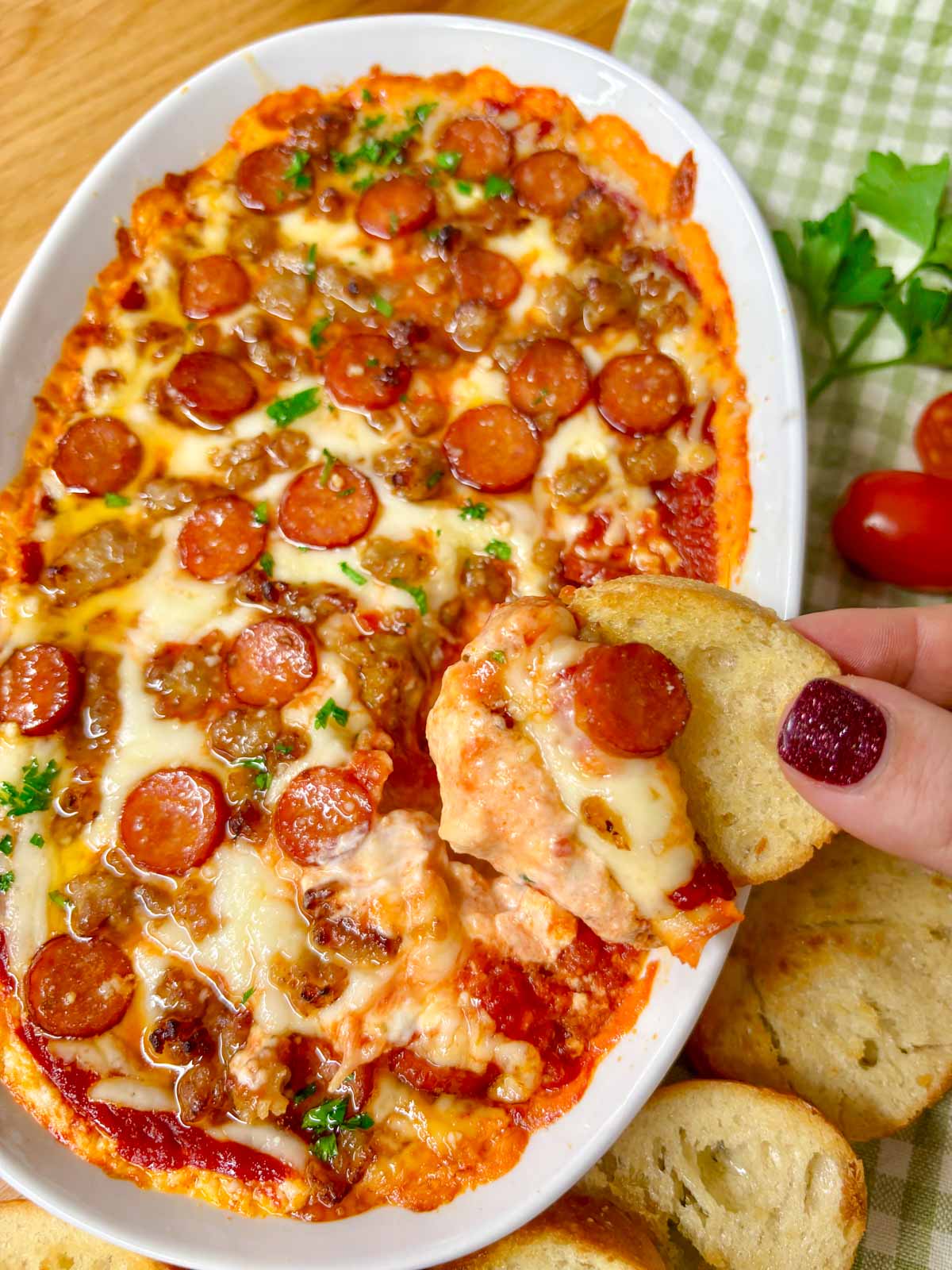 a white baking tray is filled with hot honey pepperoni sausage pizza dip. a piece of baguette is dipped in