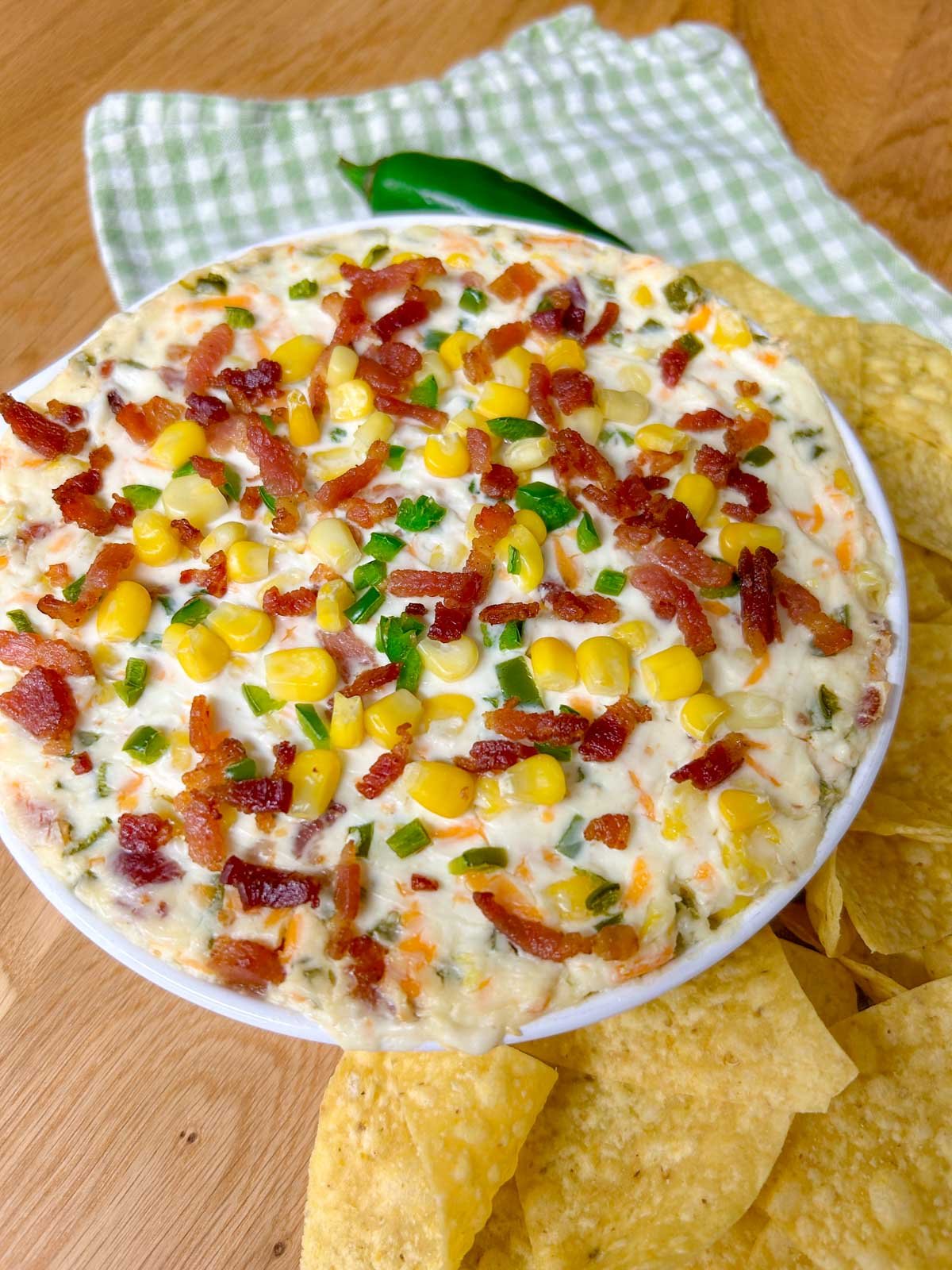 a baking dish is filled with jalapeno popper corn dip and garnished with jalapenos, bacon and corn. 