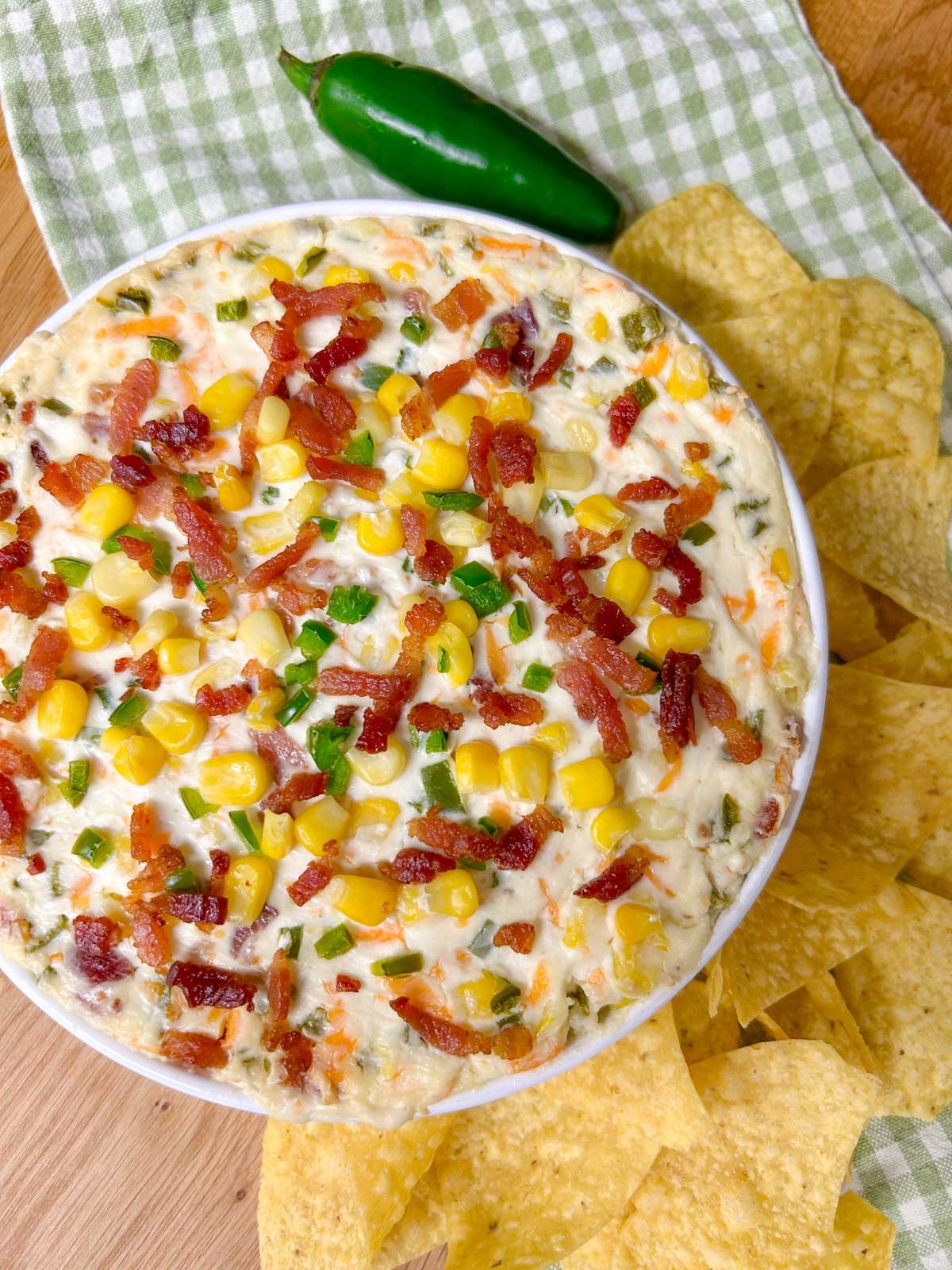 a baking dish is filled with jalapeno popper corn dip and garnished with jalapenos, bacon and corn. 