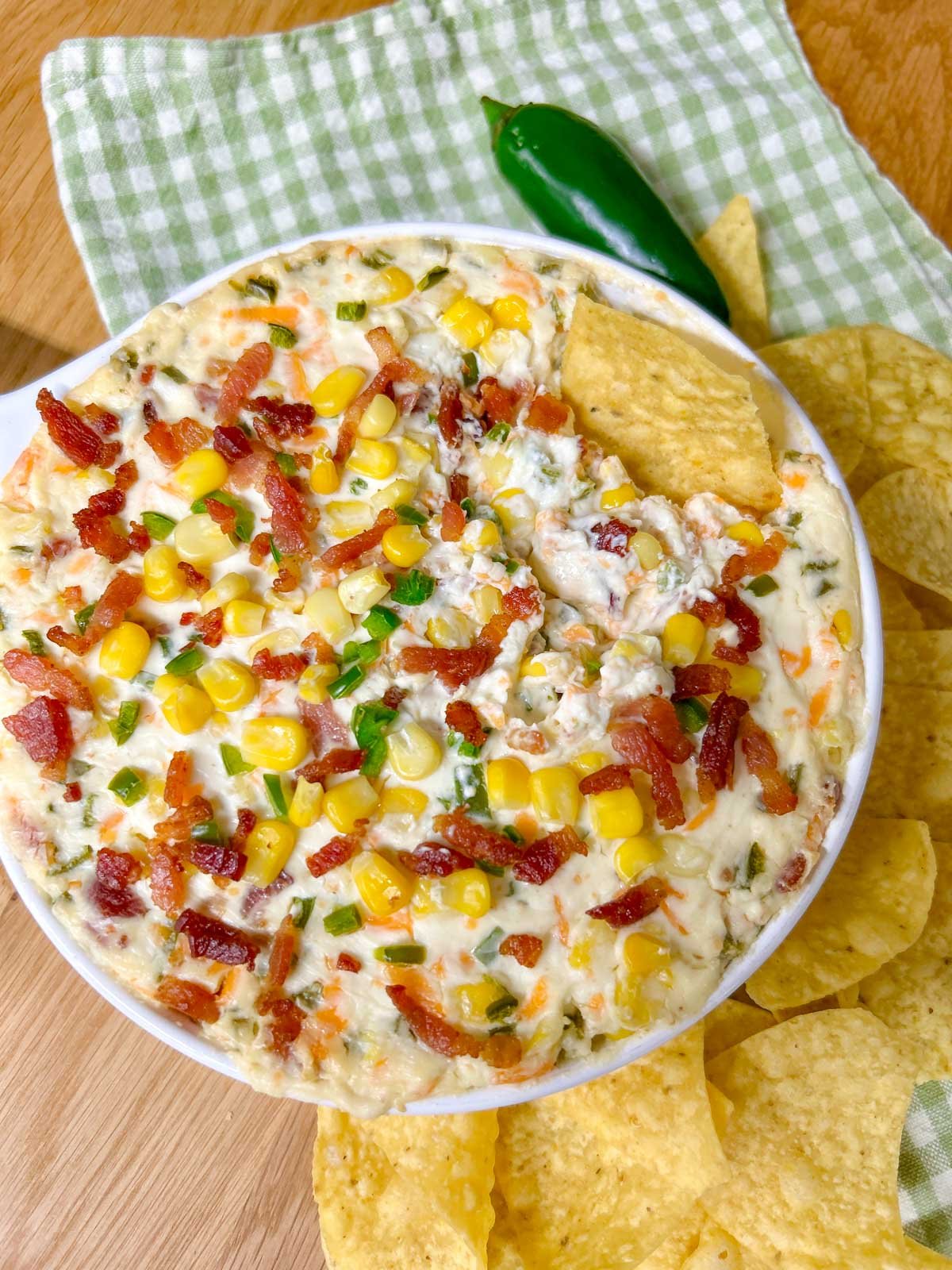 a baking dish is filled with jalapeno popper corn dip and garnished with jalapenos, bacon and corn.  one chip is dipped