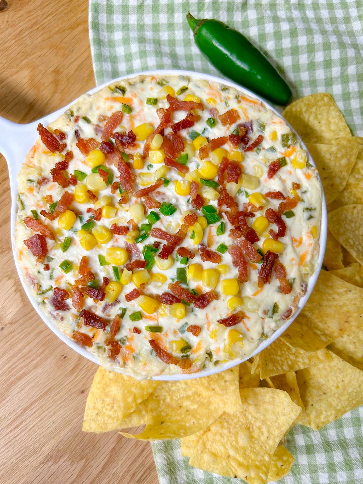 a baking dish is filled with jalapeno popper corn dip and garnished with jalapenos, bacon and corn. 