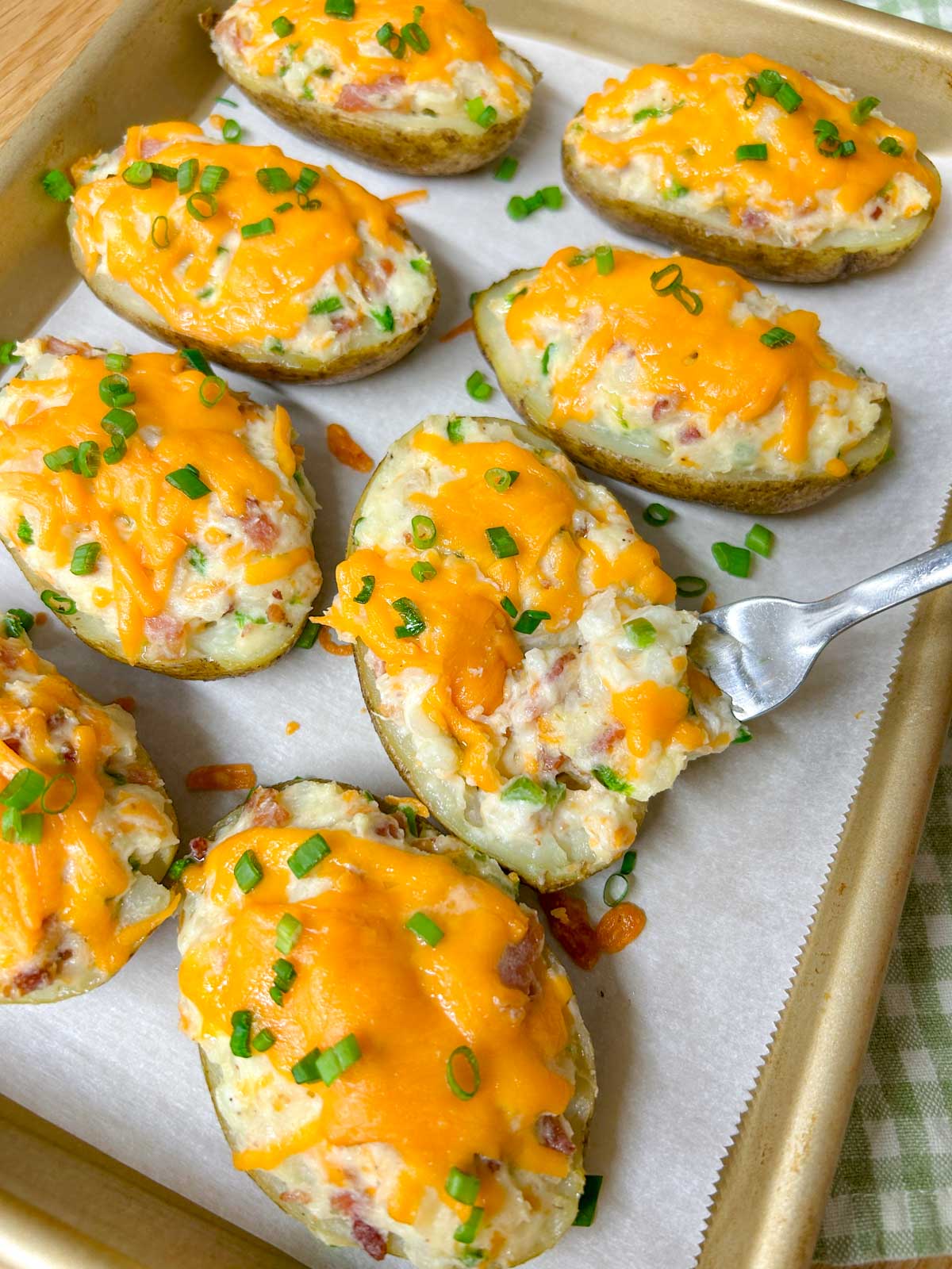 a baking tray is filled with 8 jalapeno popper twice baked potatoes and garnished with green onions. a fork cuts the potato.