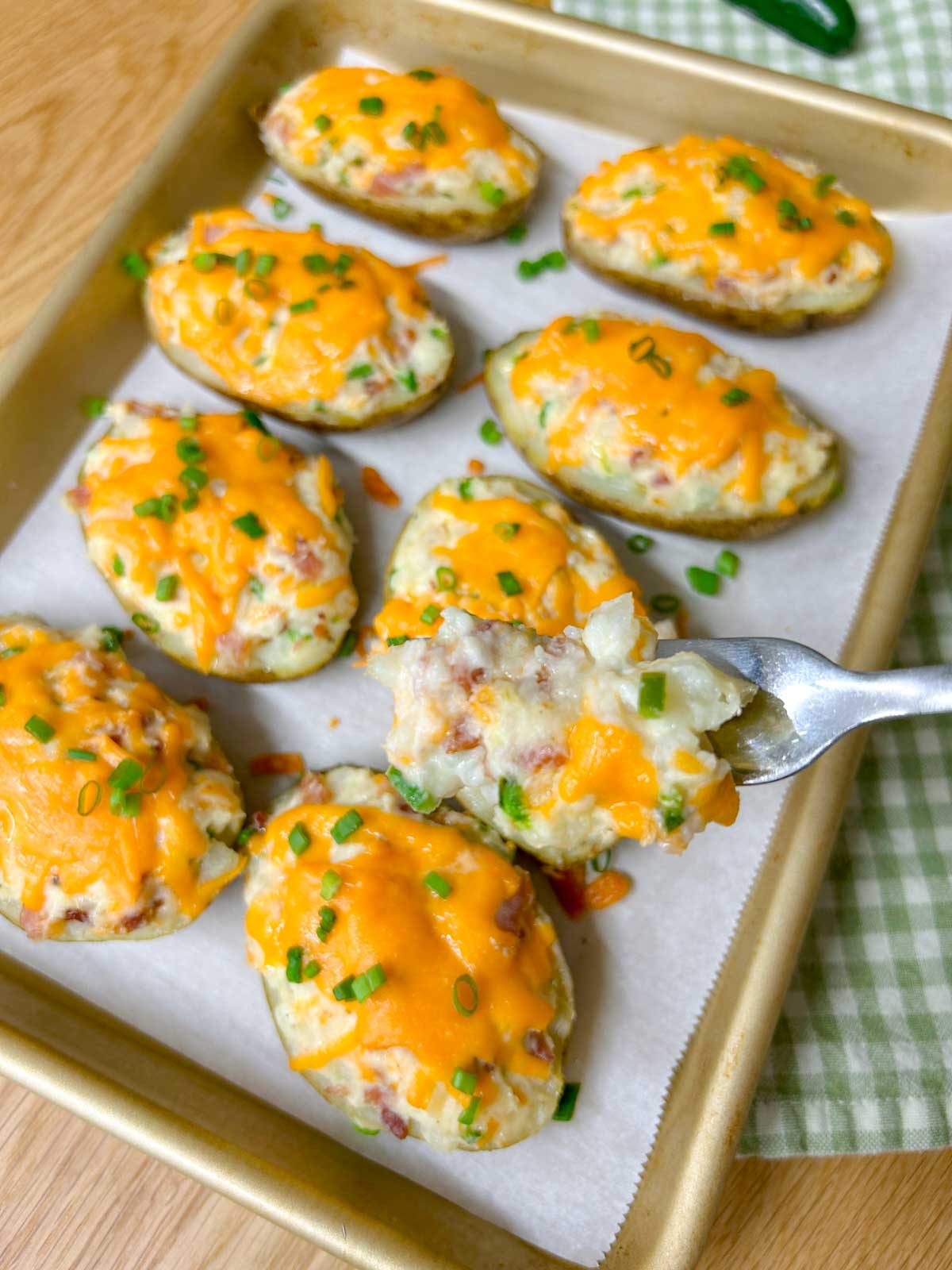 a baking tray is filled with 8 jalapeno popper twice baked potatoes and garnished with green onions. a fork is held close to camear.