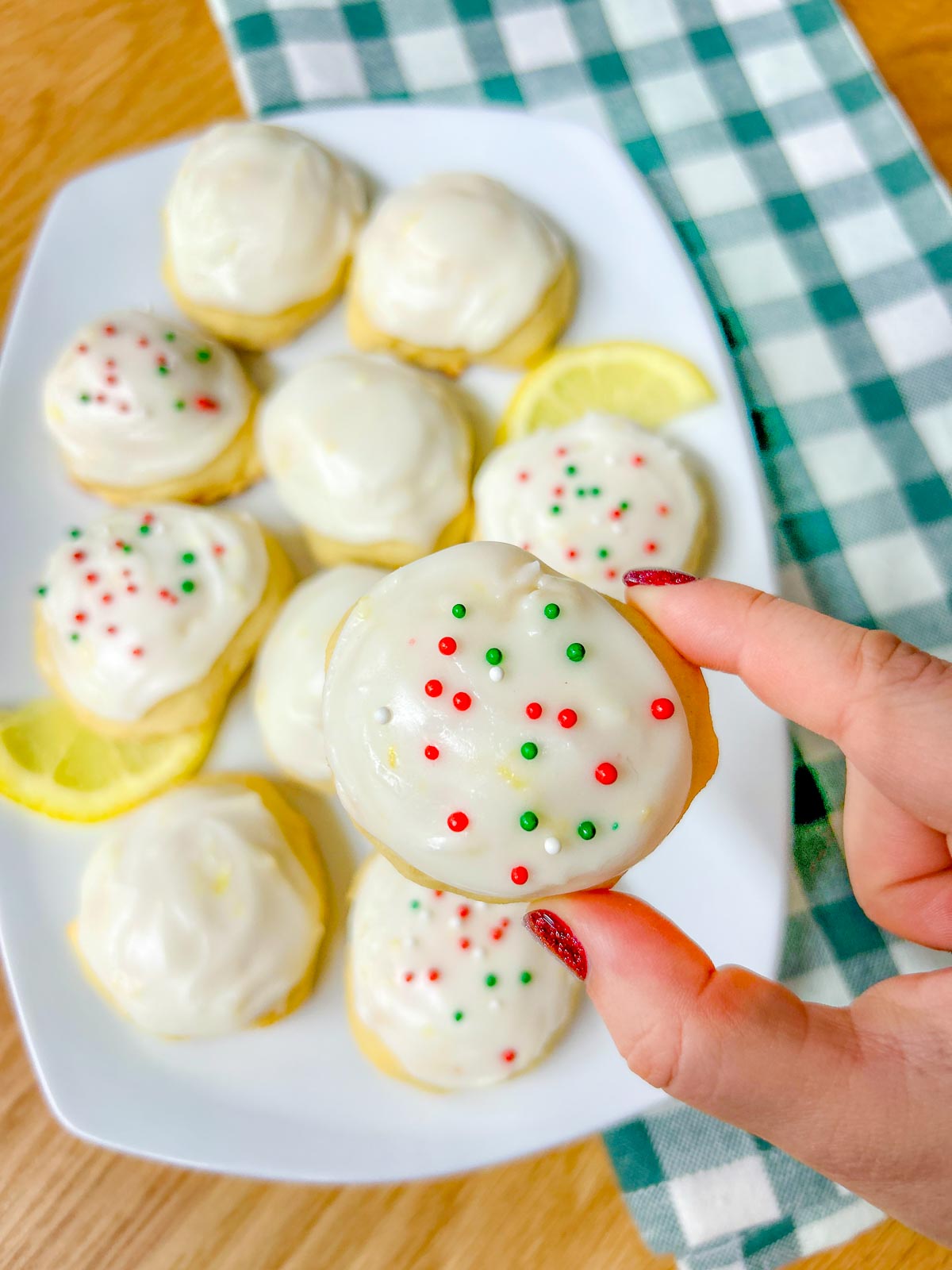 a white plate is filled with Italian lemon ricotta cookies, some have sprinkles and lemons garnish the plate
