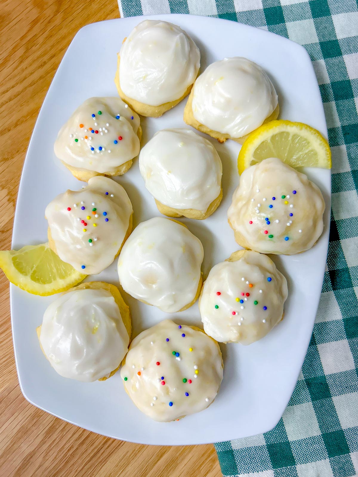 a white plate is filled with Italian lemon ricotta cookies, some have sprinkles and lemons garnish the plate