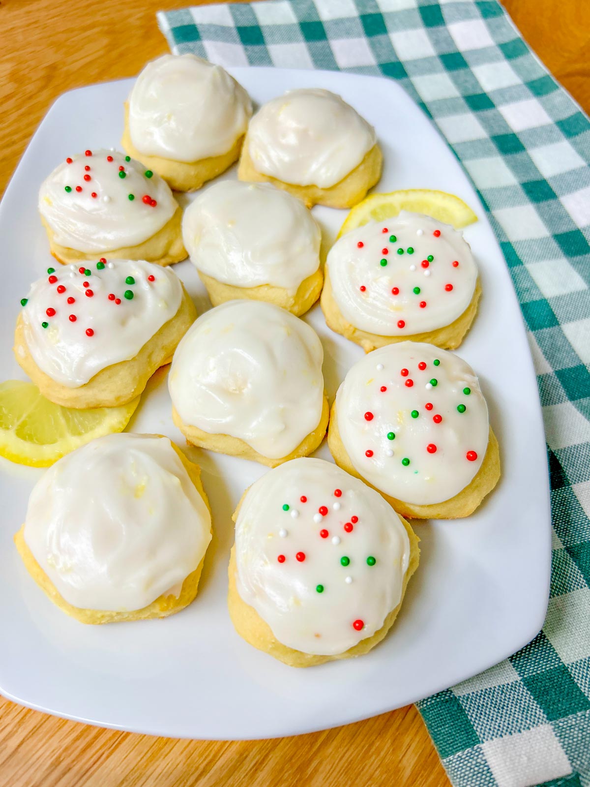 a white plate is filled with Italian lemon ricotta cookies, some have sprinkles and lemons garnish the plate