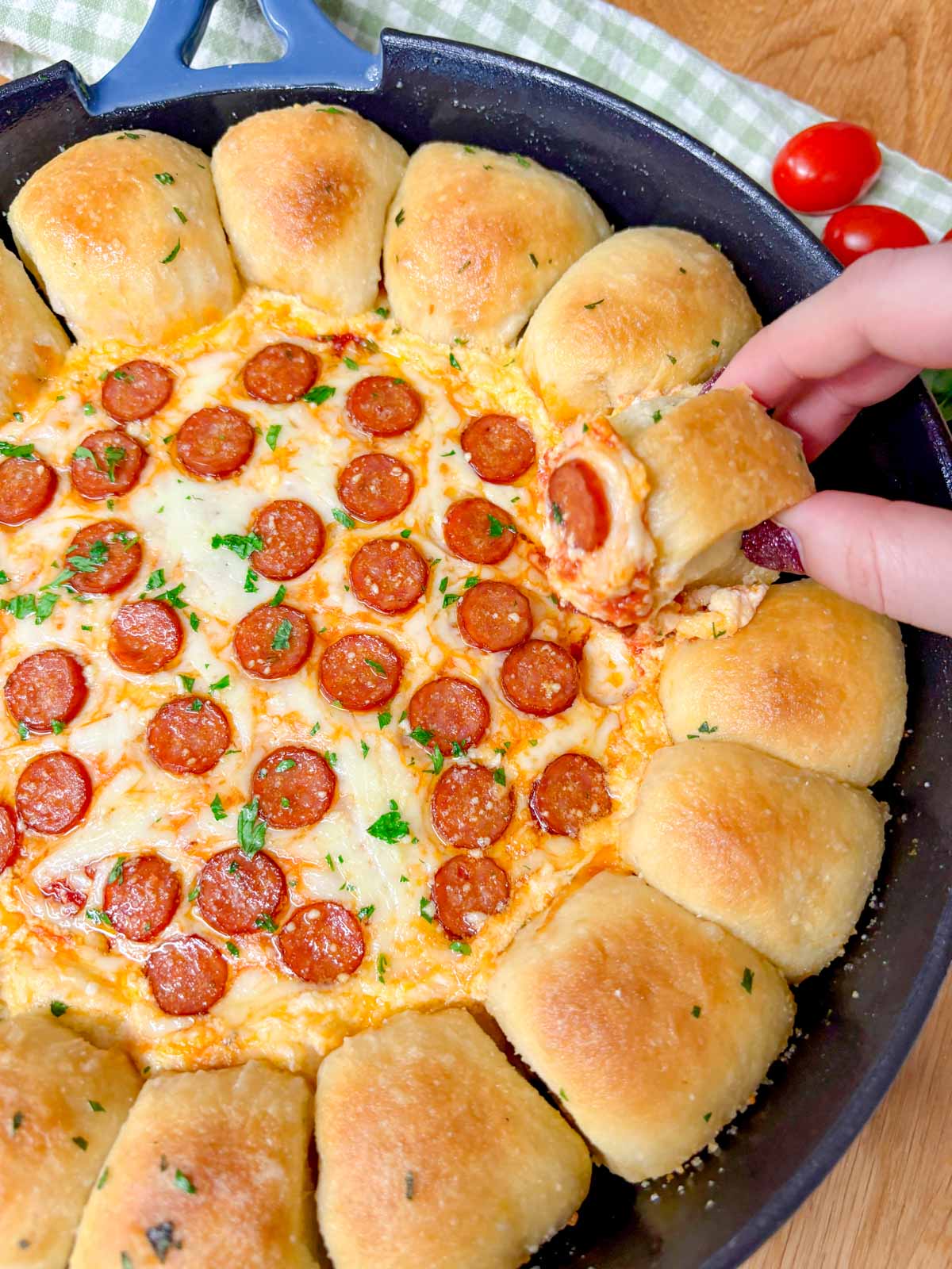 a pizza dip ring with pizza dough balls and a pizza dip in the middle is in a cast iron skillet. one piece of bread is dipped