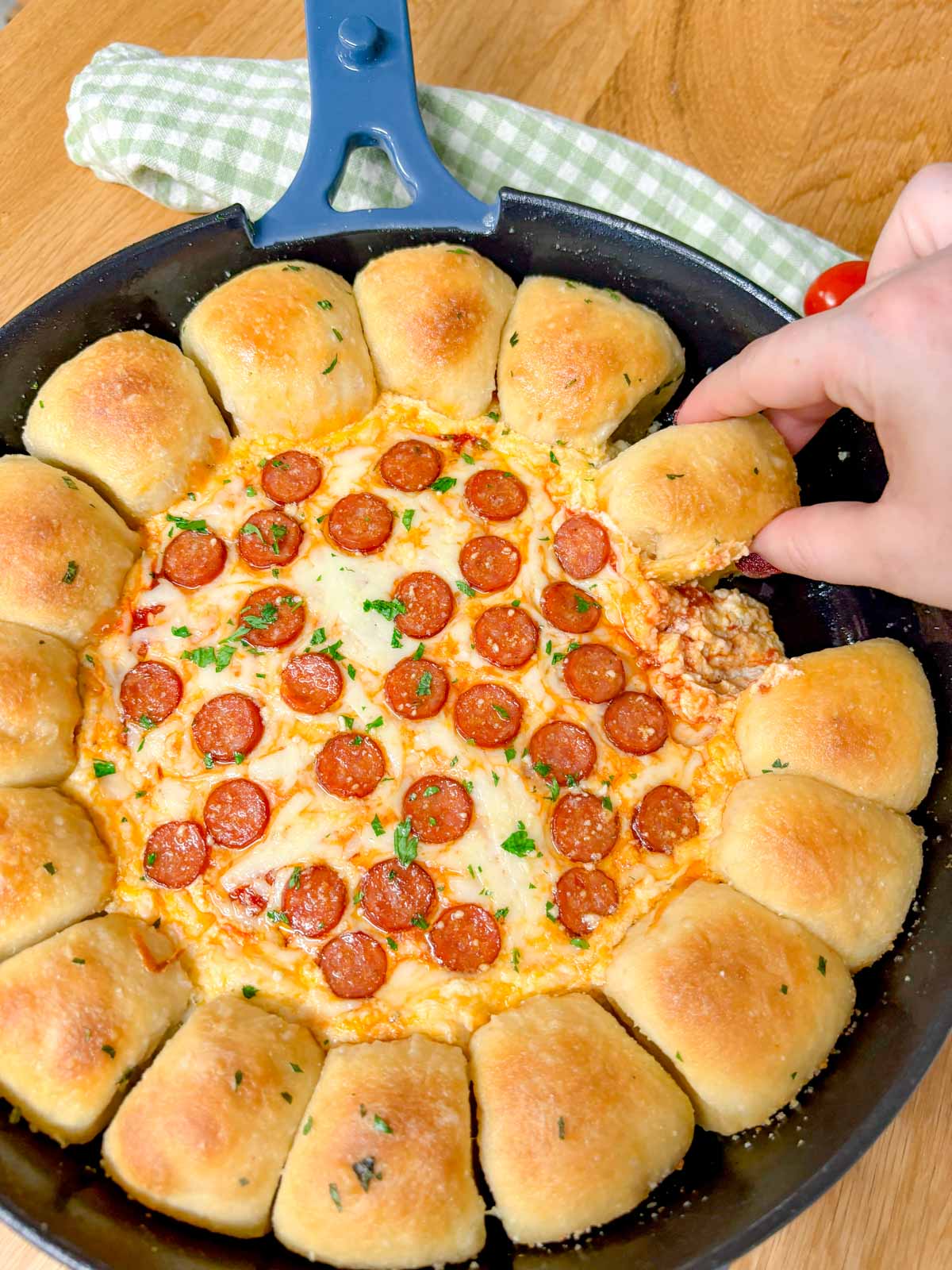 a pizza dip ring with pizza dough balls and a pizza dip in the middle is in a cast iron skillet. one piece of dough is dipped