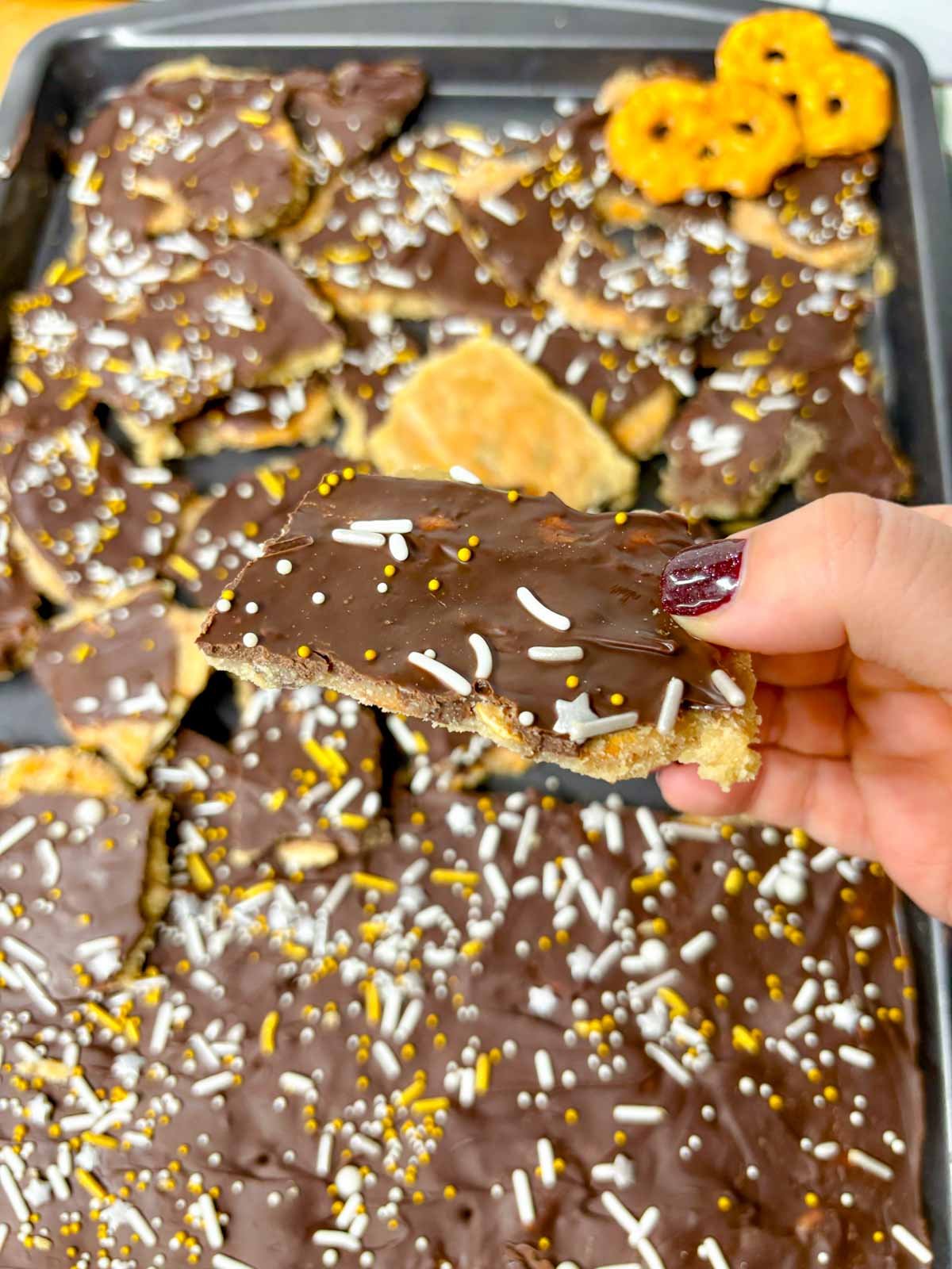 a baking tray is filled with pretzel Christmas crack. a piece is held close to camera