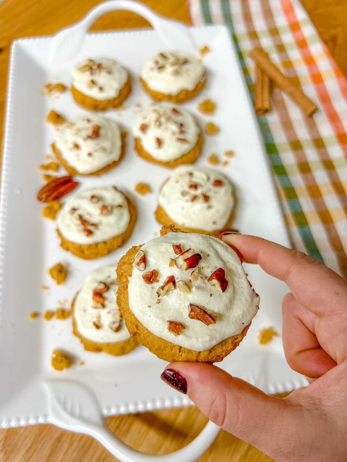 one whole pumpkin cookie is held close to camera. the plate of cookies is in the background