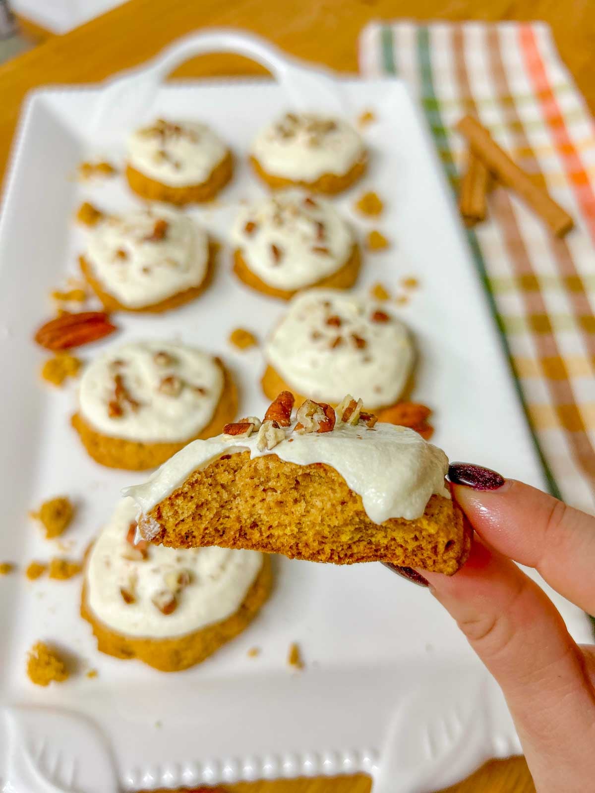 one cream cheese frosted pumpkin cookie is broken in half and held close to camera