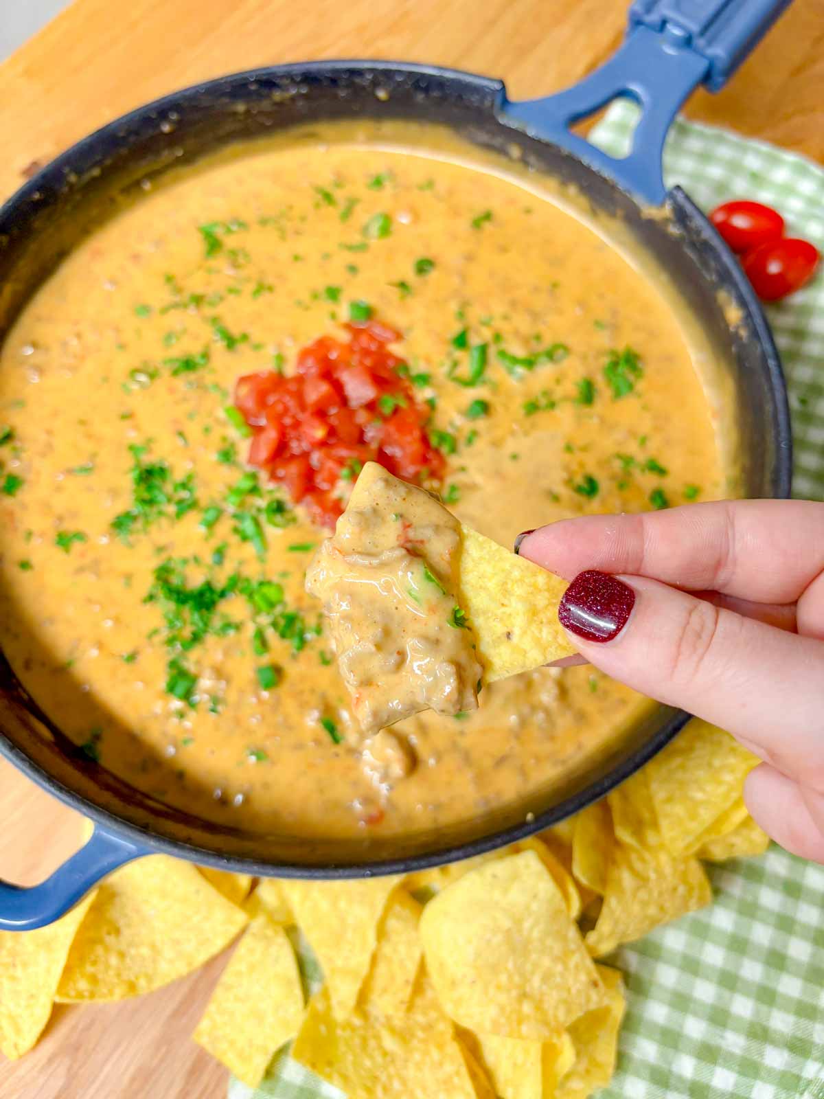 a cast iron skillet is filled with rotel dip and garnished with tomatoes and cilantro. a chip is dipped and held close to camera