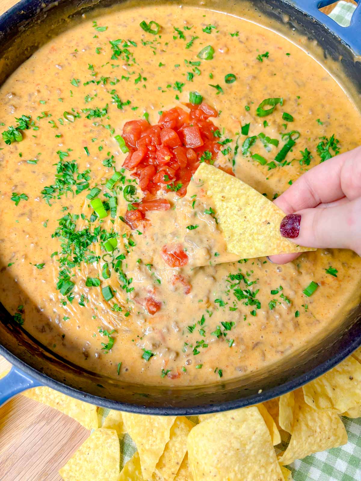 a cast iron skillet is filled with rotel dip and garnished with tomatoes and cilantro. a tortilla chip is dipped in.