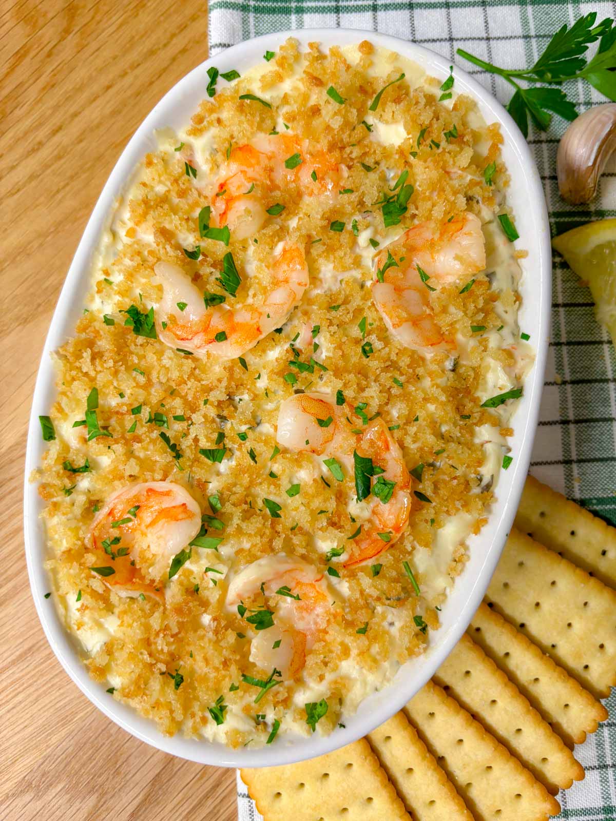 a white baking dish is filled with shrimp dip and garnished with breadcrumbs and parsley