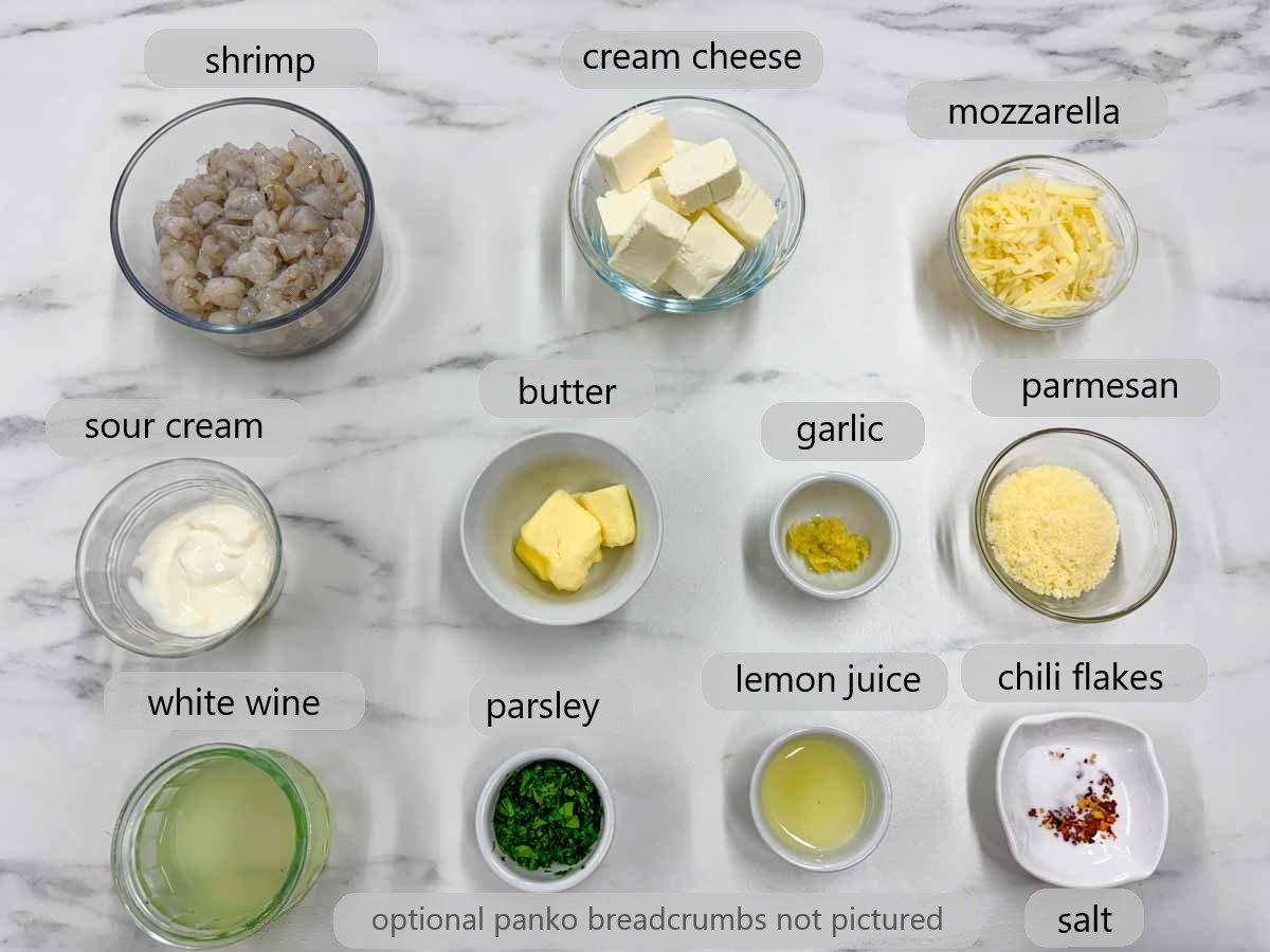 bowls with ingredients on a counter and text overlay reading shrimp, cream cheese, mozzarella, sour cream, butter, garlic, parmesan, white wine, parsley, lemon juice, chili flakes and salt.