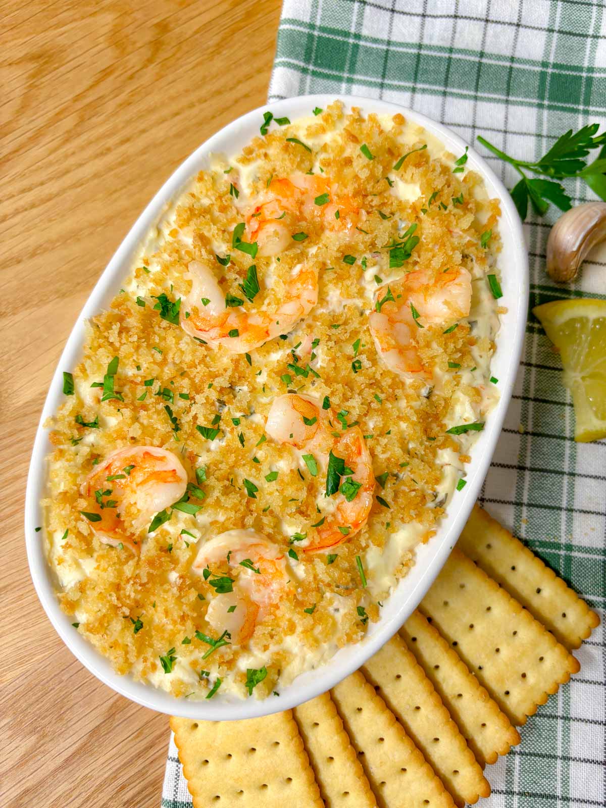 a white baking dish is filled with shrimp dip and garnished with breadcrumbs and parsley
