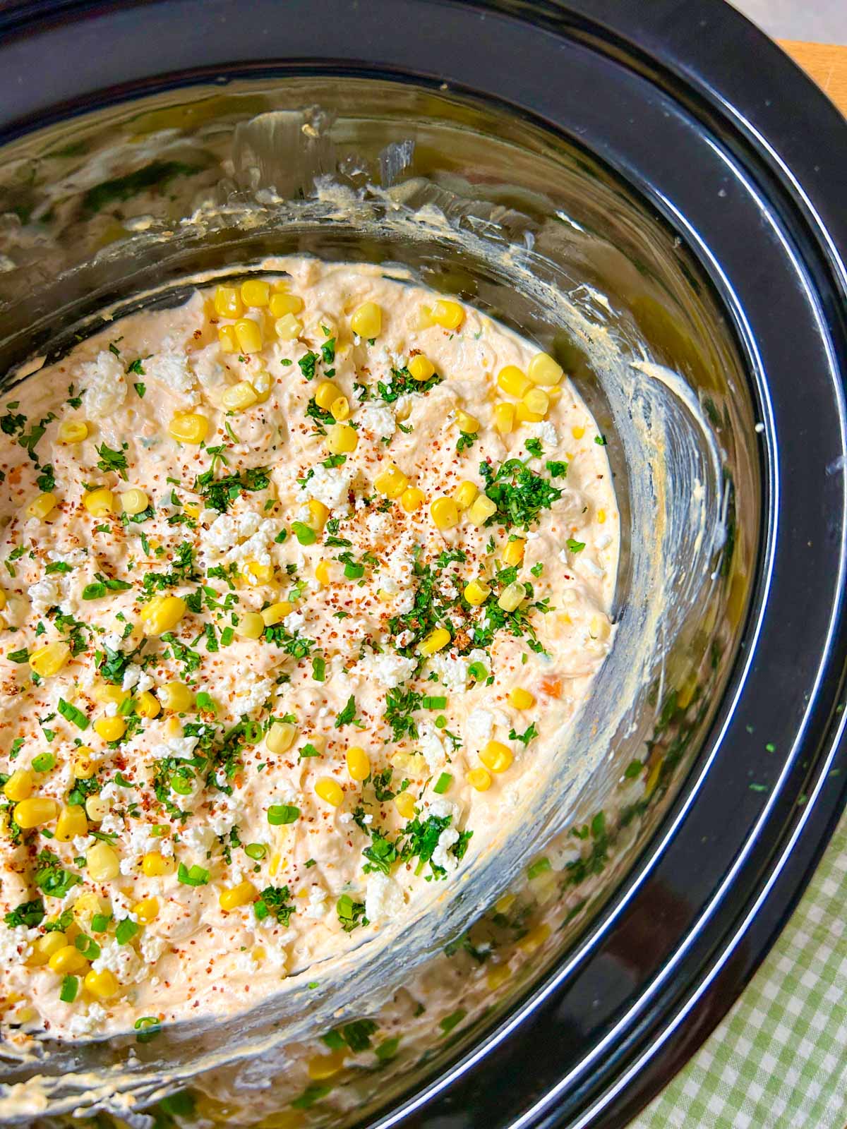 a slow cooker is filled with street corn dip and garnished with cilantro, corn and cotija cheese.