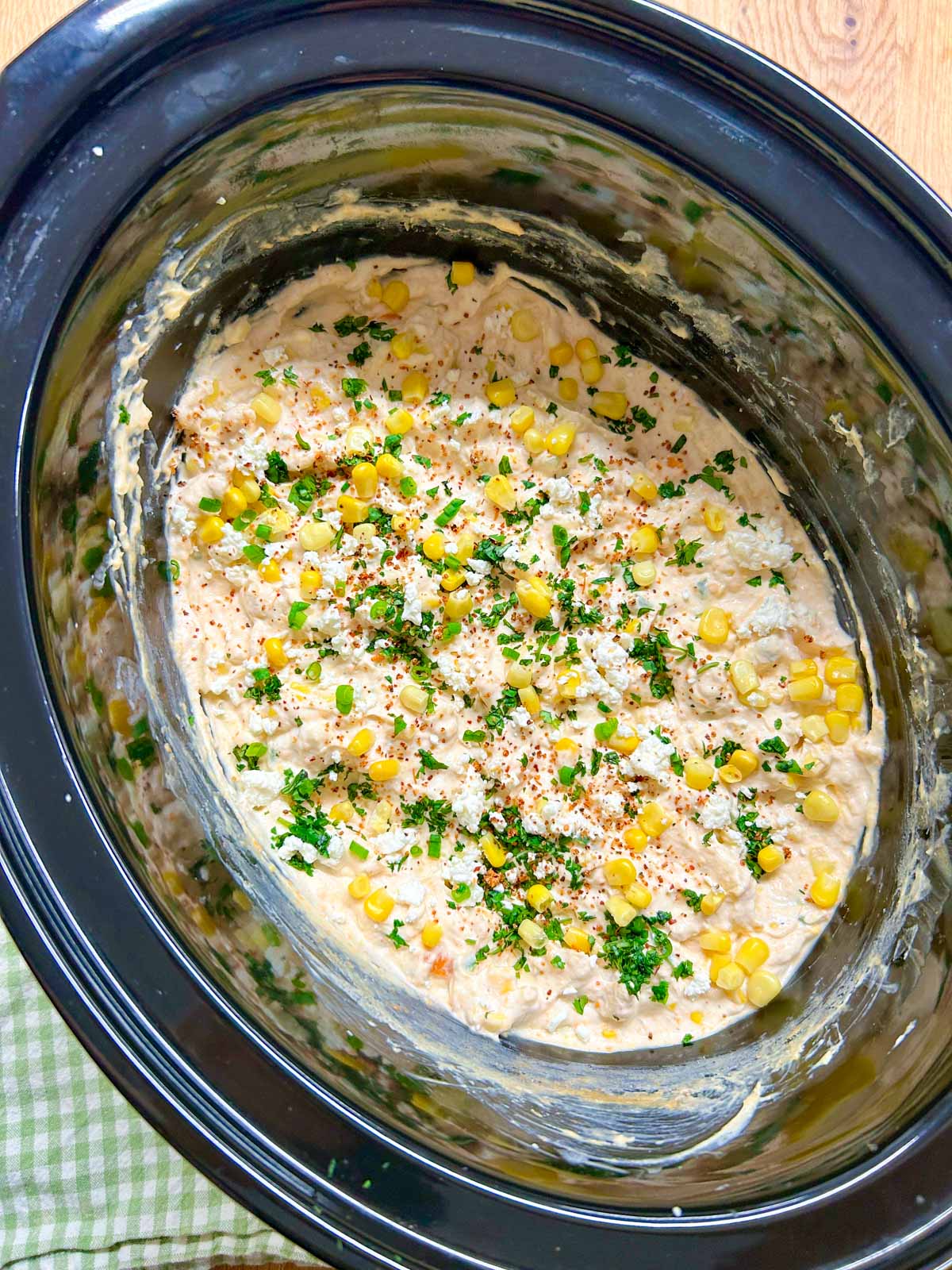 a slow cooker is filled with street corn dip and garnished with cilantro, corn and cotija cheese.