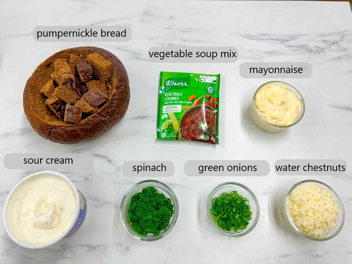 kitchen counter with bowls with ingredients and text overlays reading pumpernickel bread, vegetable soup mix, mayonnaise, sour cream, spinach, green onions and water chestnuts