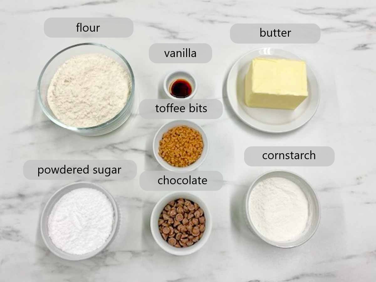 kitchen counter with ingredients and text overlays reading flour, vanilla, butter, powdered sugar, toffee bits, chocolate, and cornstarch