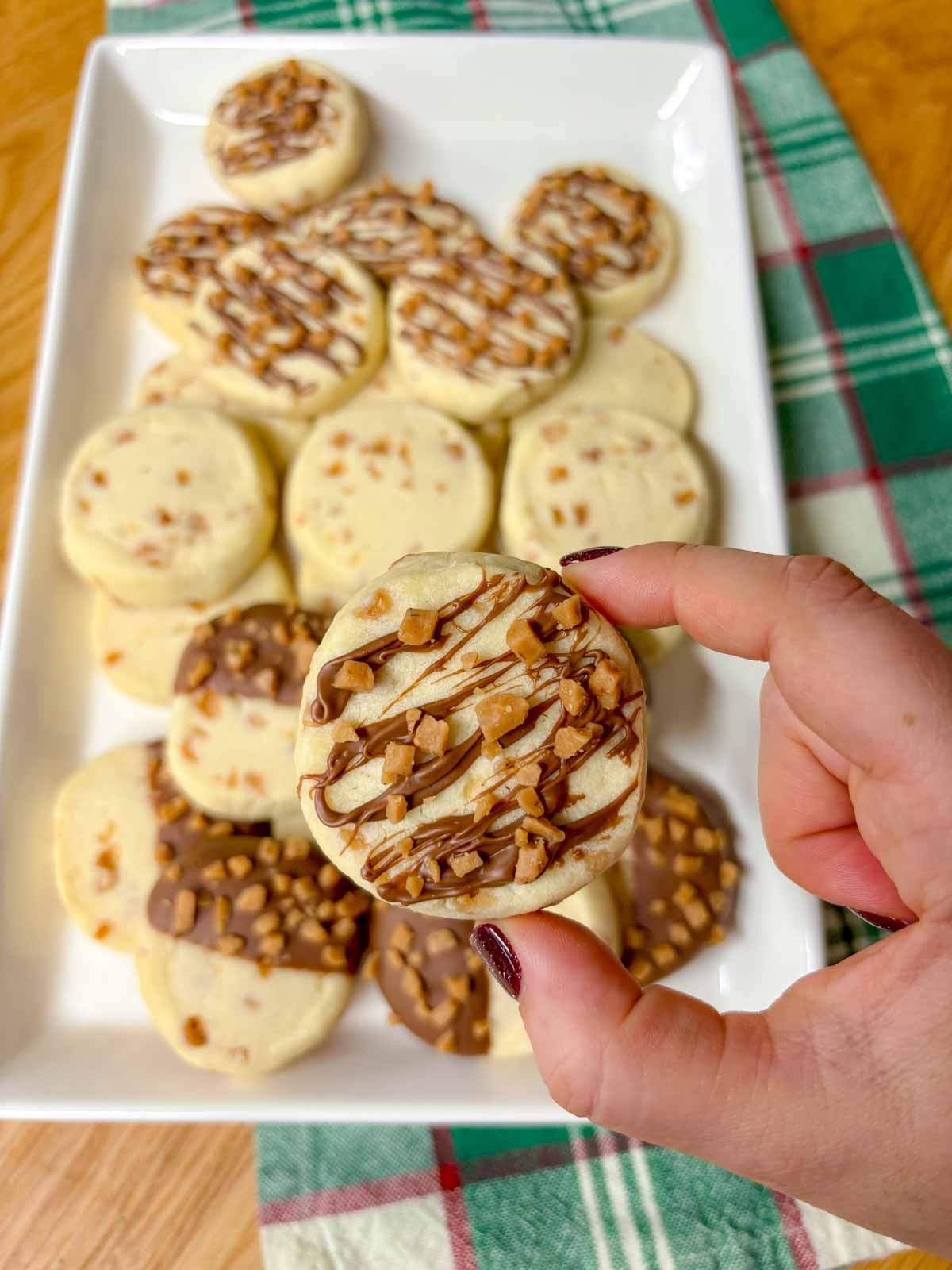 one cookie that is drizzled with chocolate and topped with toffee bits is held up to camera