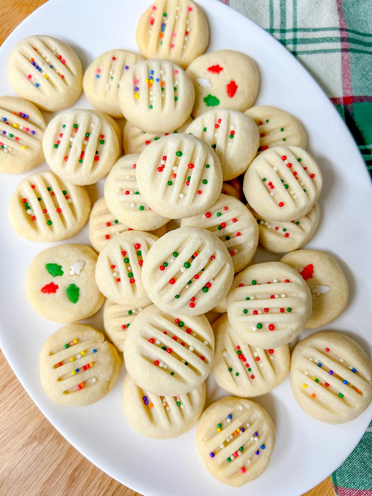 a white platter is filled with whipped shortbread cookies that are topped with sprinkles
