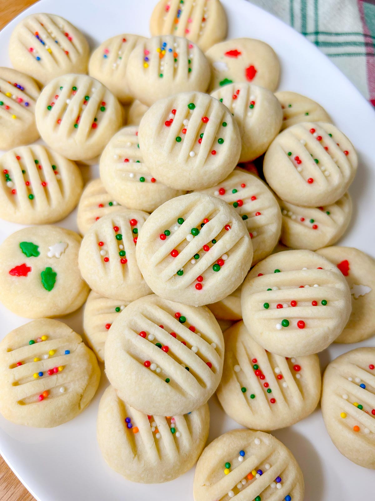 a white platter is filled with whipped shortbread cookies that are topped with sprinkles
