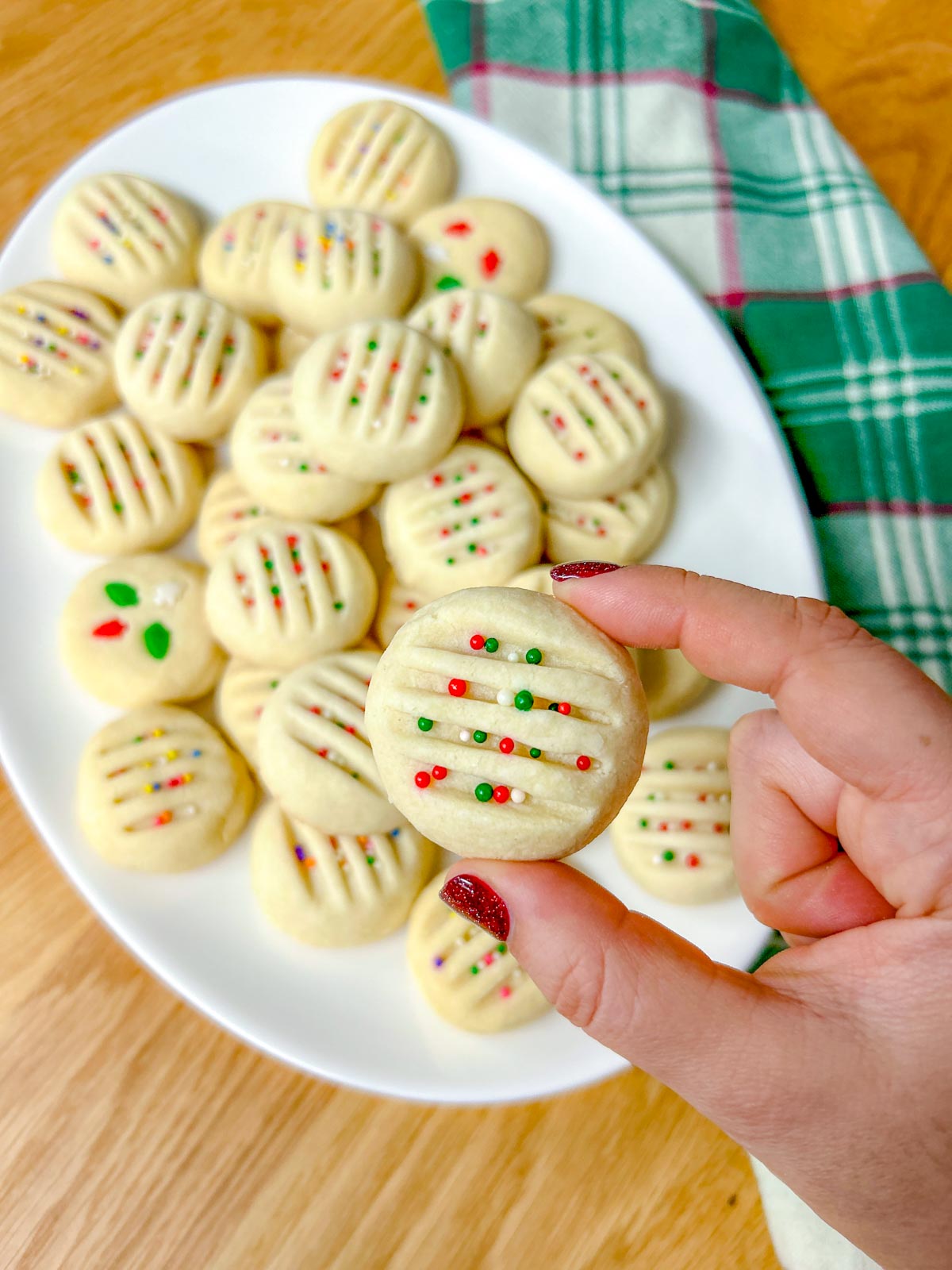 a white platter is filled with whipped shortbread cookies that are topped with sprinkles