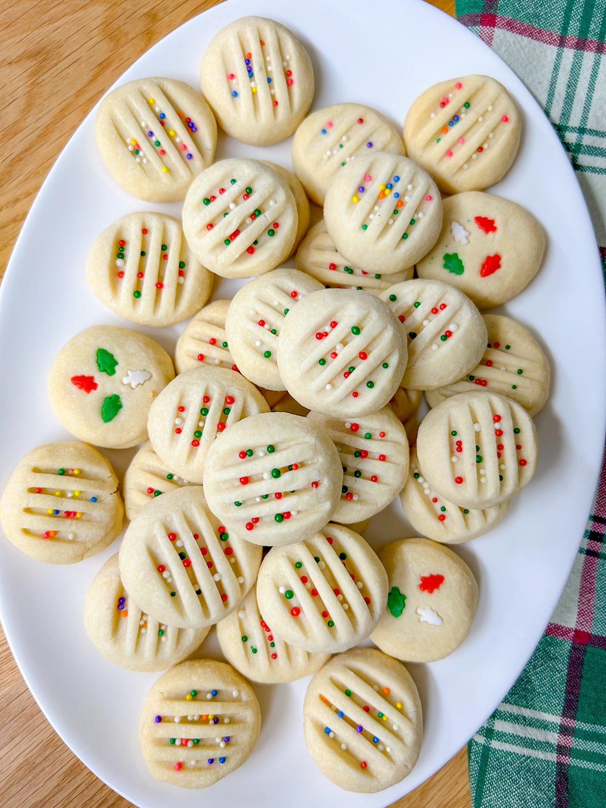a white platter is filled with whipped shortbread cookies that are topped with sprinkles