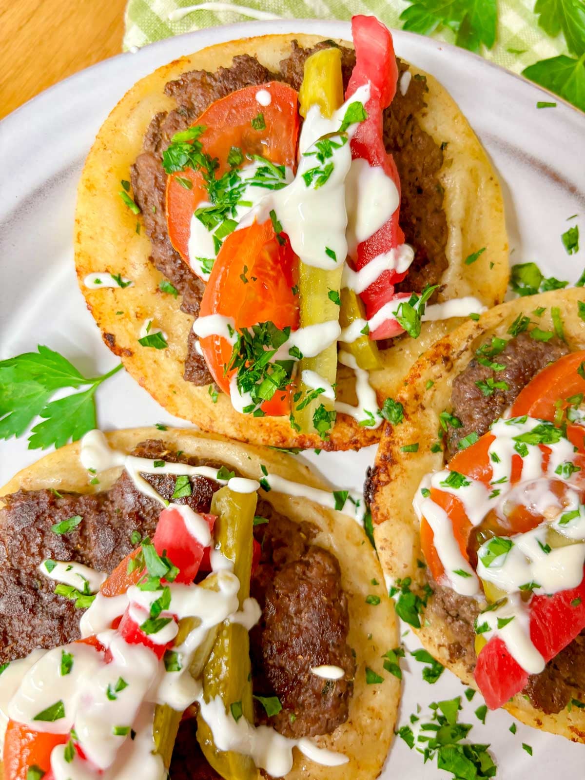 close up shot of a plate of beef kebab tacos that are drizzled with garlic sauce and topped with chopped parsley
