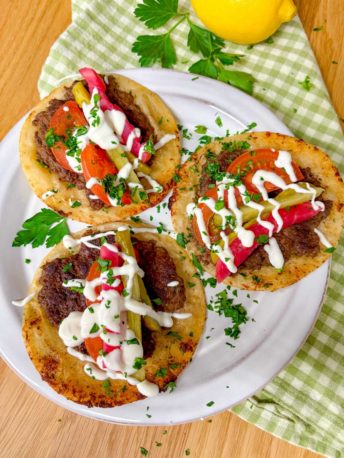 plate with three beef kebab smash tacos garnished with parsley and garlic sauce