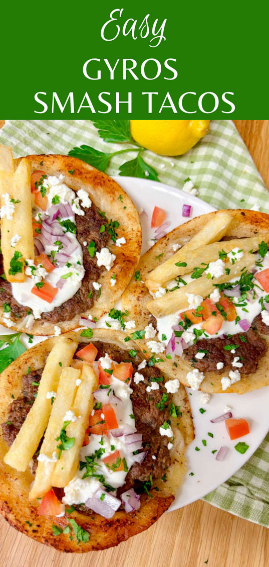 a white plate is filled with three Greek gyros smash tacos with tzatziki, fries, tomato, onion, and feta on top