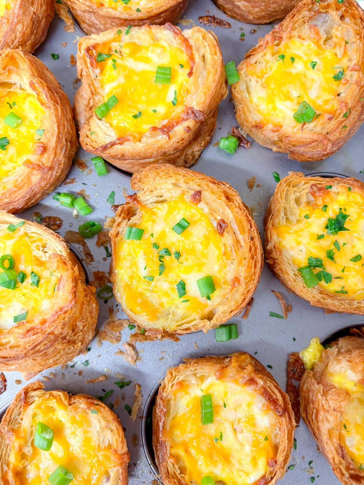 a muffin tin is filled with breakfast croissant cups and garnished with green onions and parsley