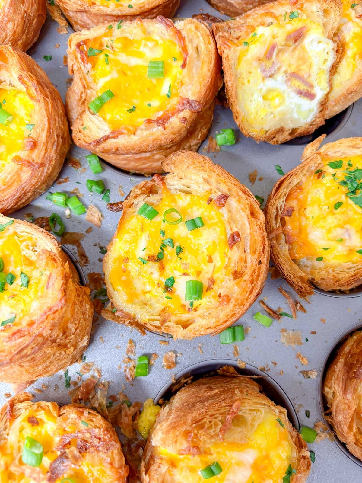 a muffin tin is filled with breakfast croissant cups and garnished with green onions and parsley