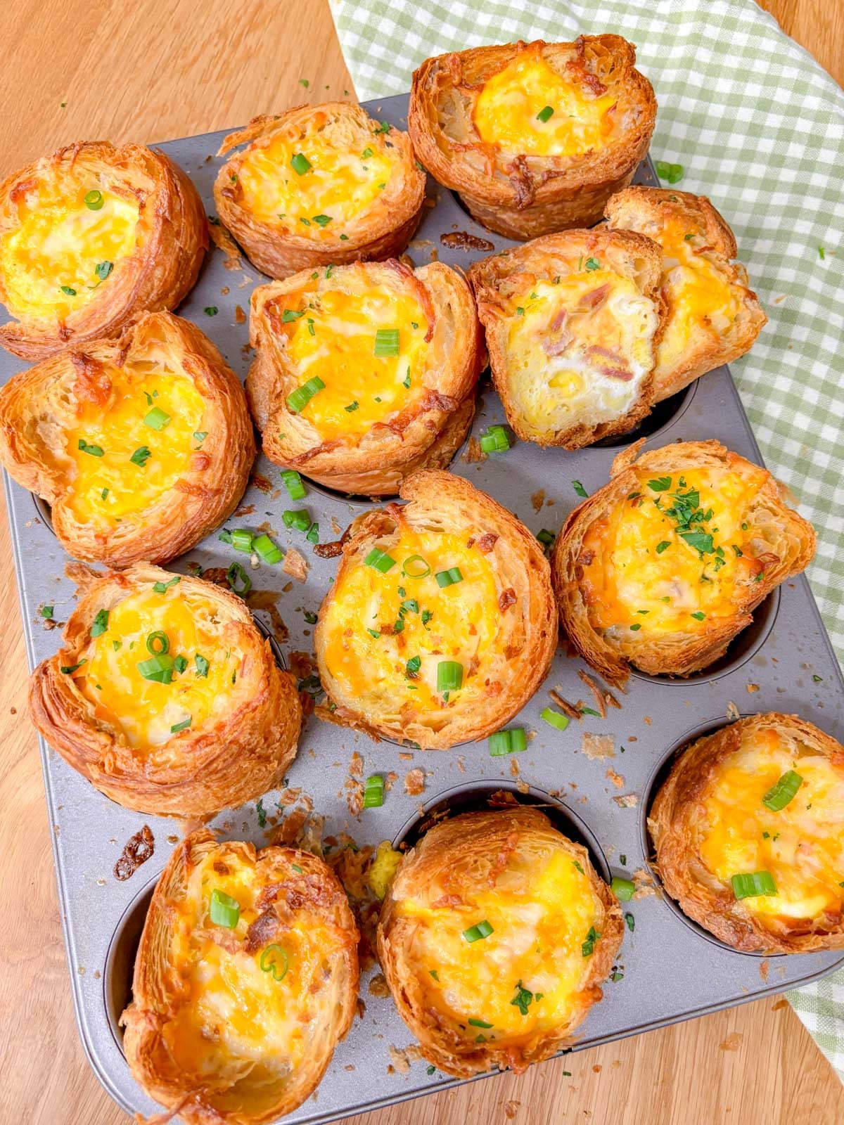 a muffin tin is filled with breakfast croissant cups and garnished with green onions and parsley. one is cut in half