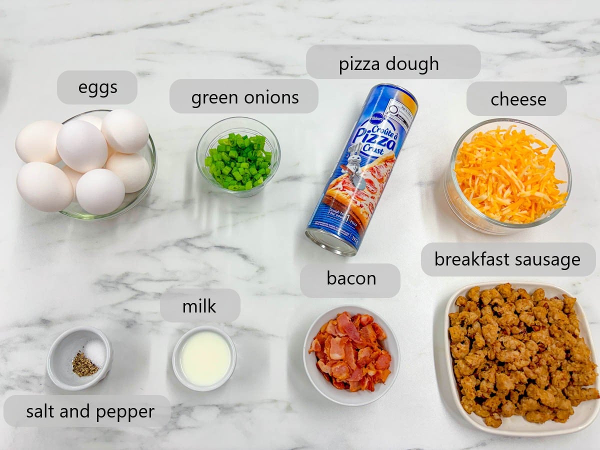 kitchen counter with bowls of ingredients and text overlays reading eggs, green onions, pizza dough, cheese, salt and pepper, milk, bacon, and breakfast sausage.