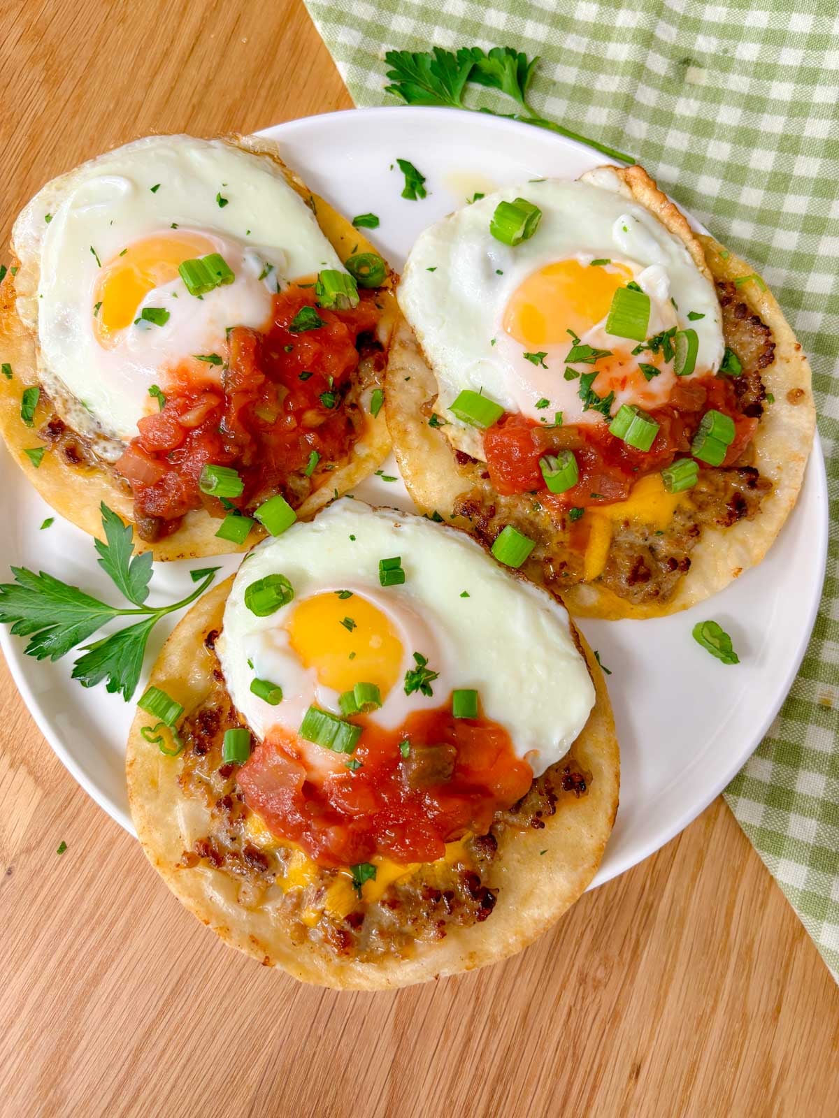 a white plate has three breakfast smash tacos on it garnished with salsa and green onions