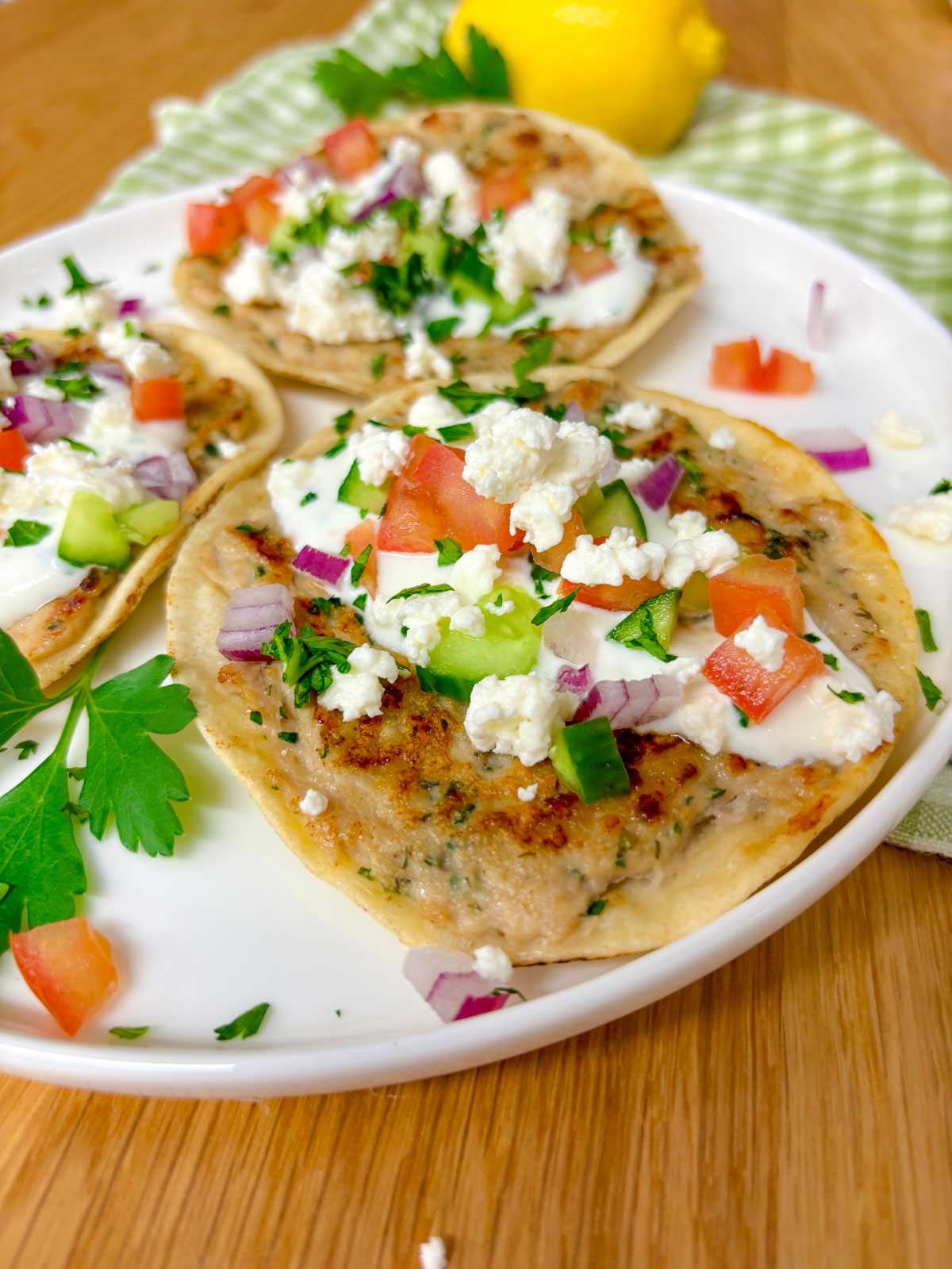 a plate is filled with three greek chicken smash tacos topped with tzatziki, onion, tomato, cucumber, onion, feta, and parsley