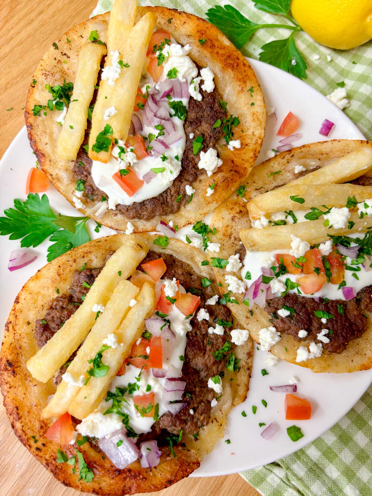 a white plate is filled with three Greek gyros smash tacos with tzatziki, fries, tomato, onion, and feta on top