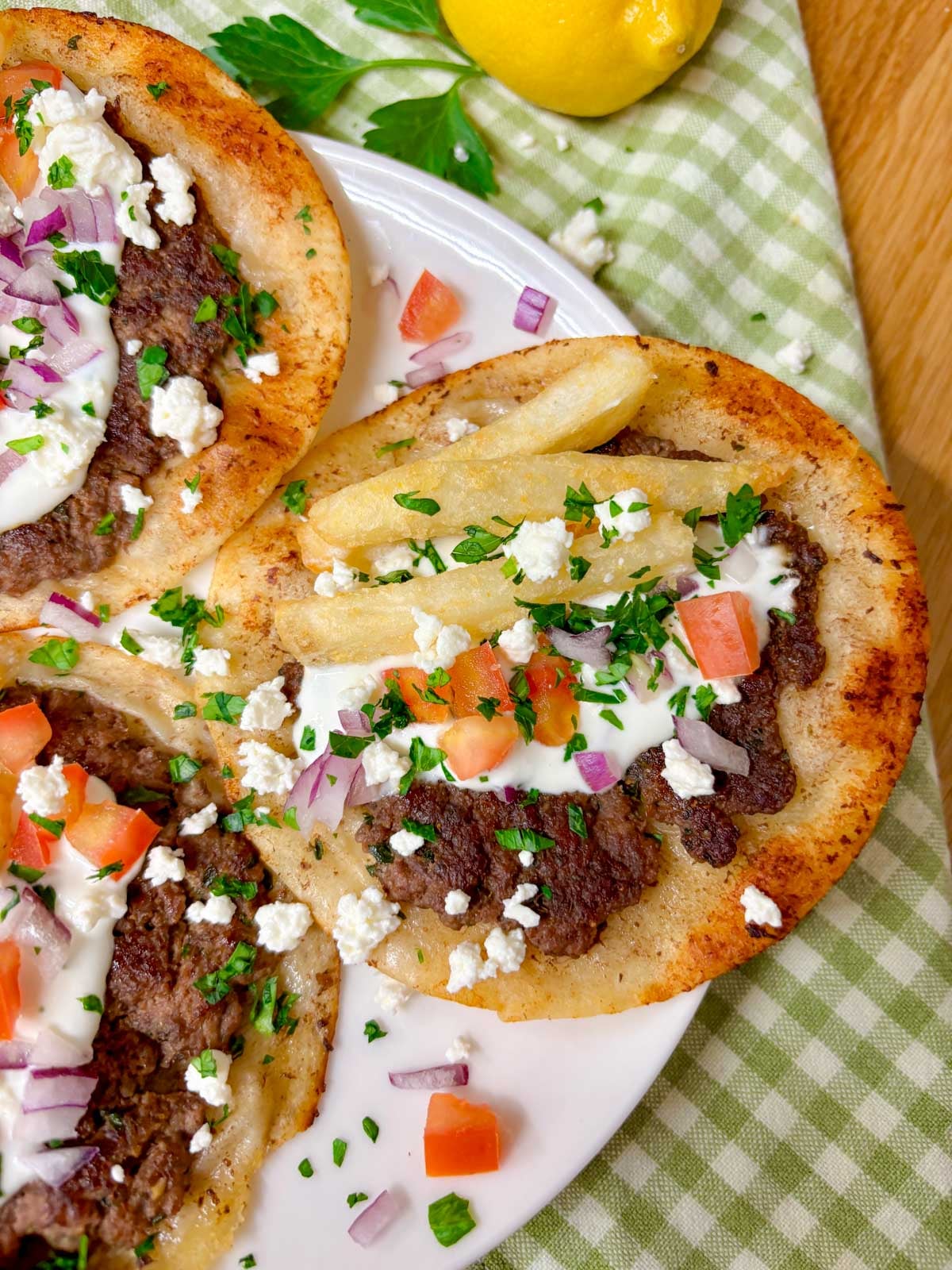 a white plate is filled with three Greek gyros smash tacos with tzatziki, fries, tomato, onion, and feta on top
