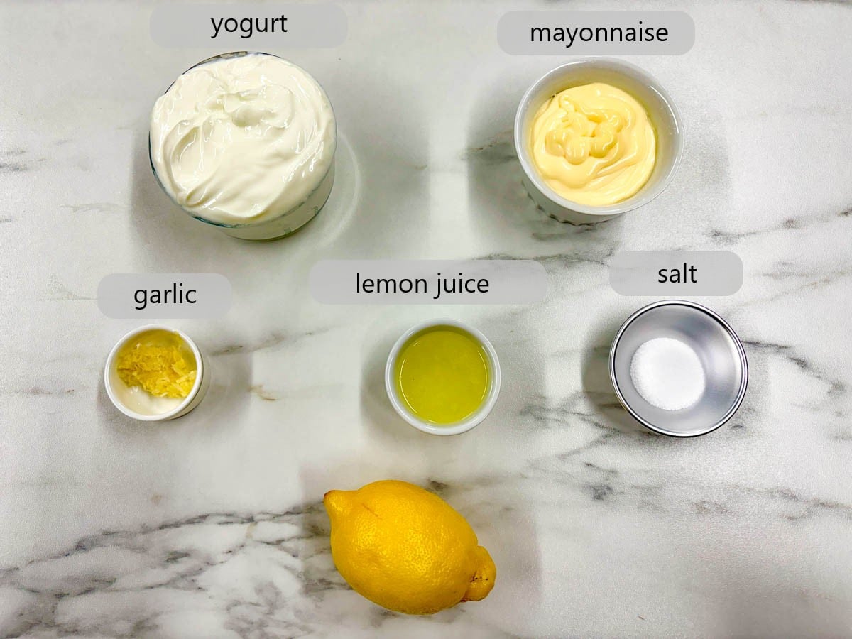 kitchen counter with bowls of ingredients with text overlays reading yogurt, mayonnaise, garlic, lemon juice, and salt.